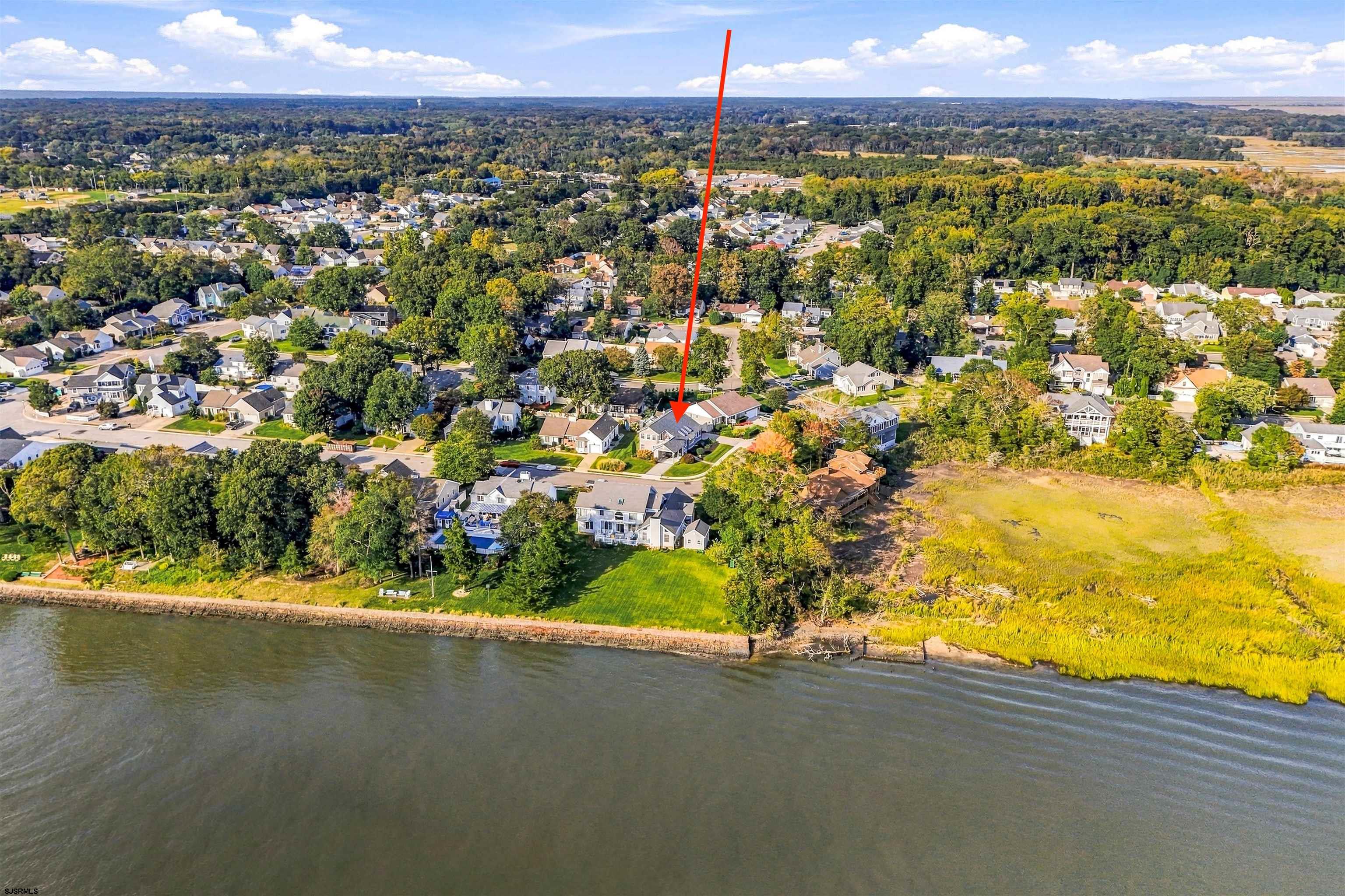 Aerial view of the waterfront home marked by a red arrow, with neighboring homes and shoreline nearby.