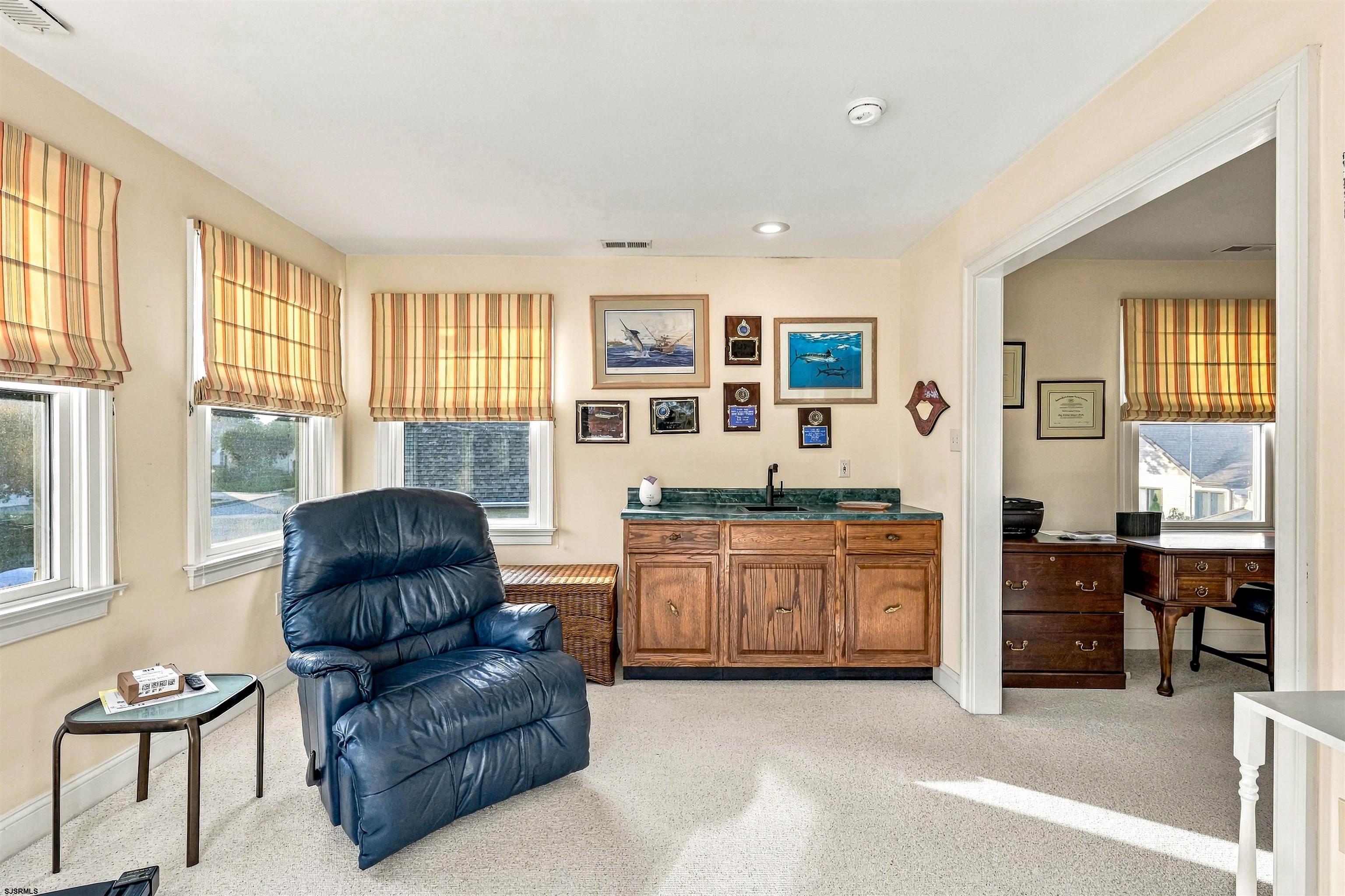 Furnished den with a blue leather recliner, striped window shades, and a wood wet bar.