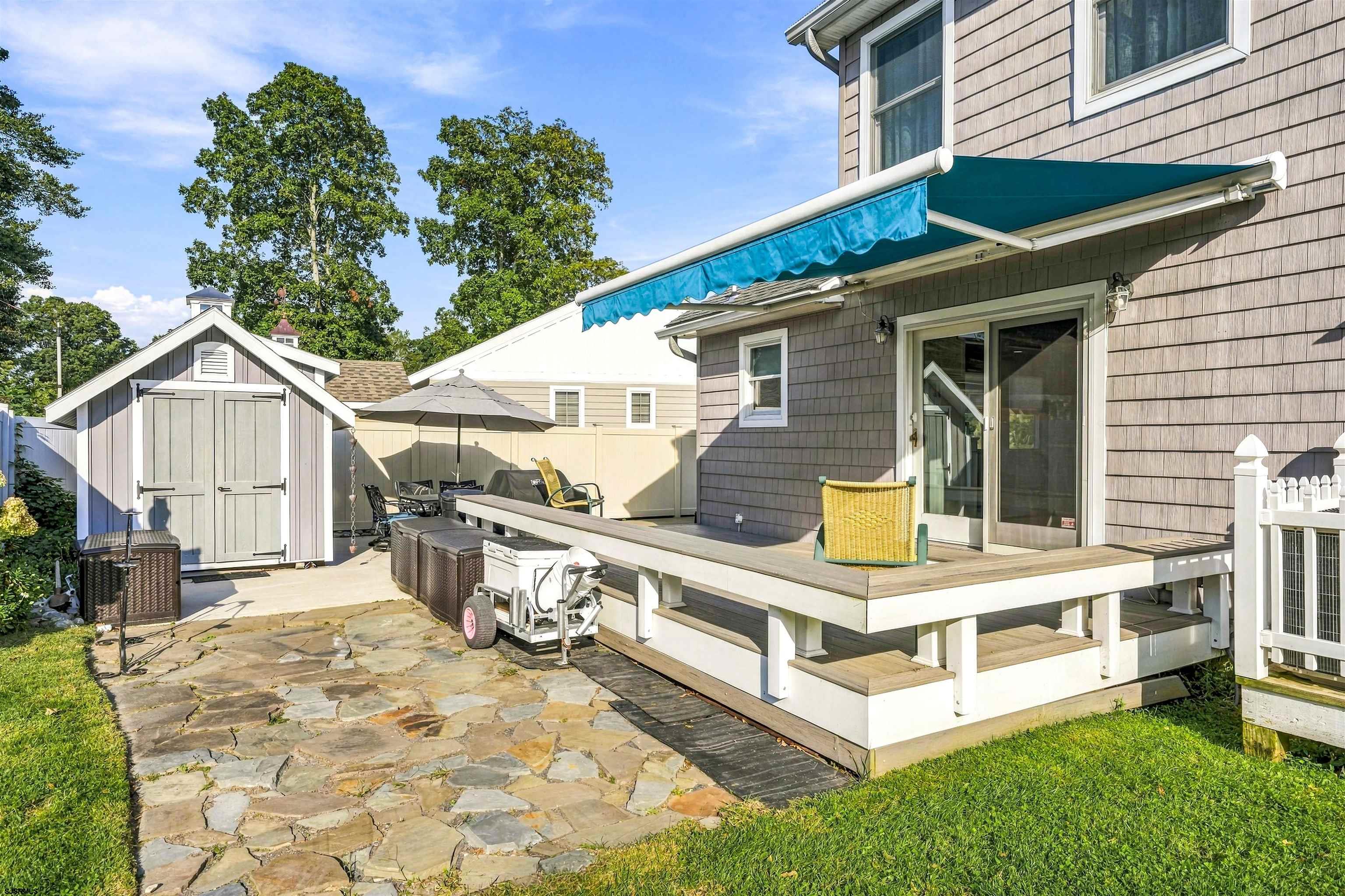 Rear patio with raised deck, blue awning, stone paving, and detached shed.