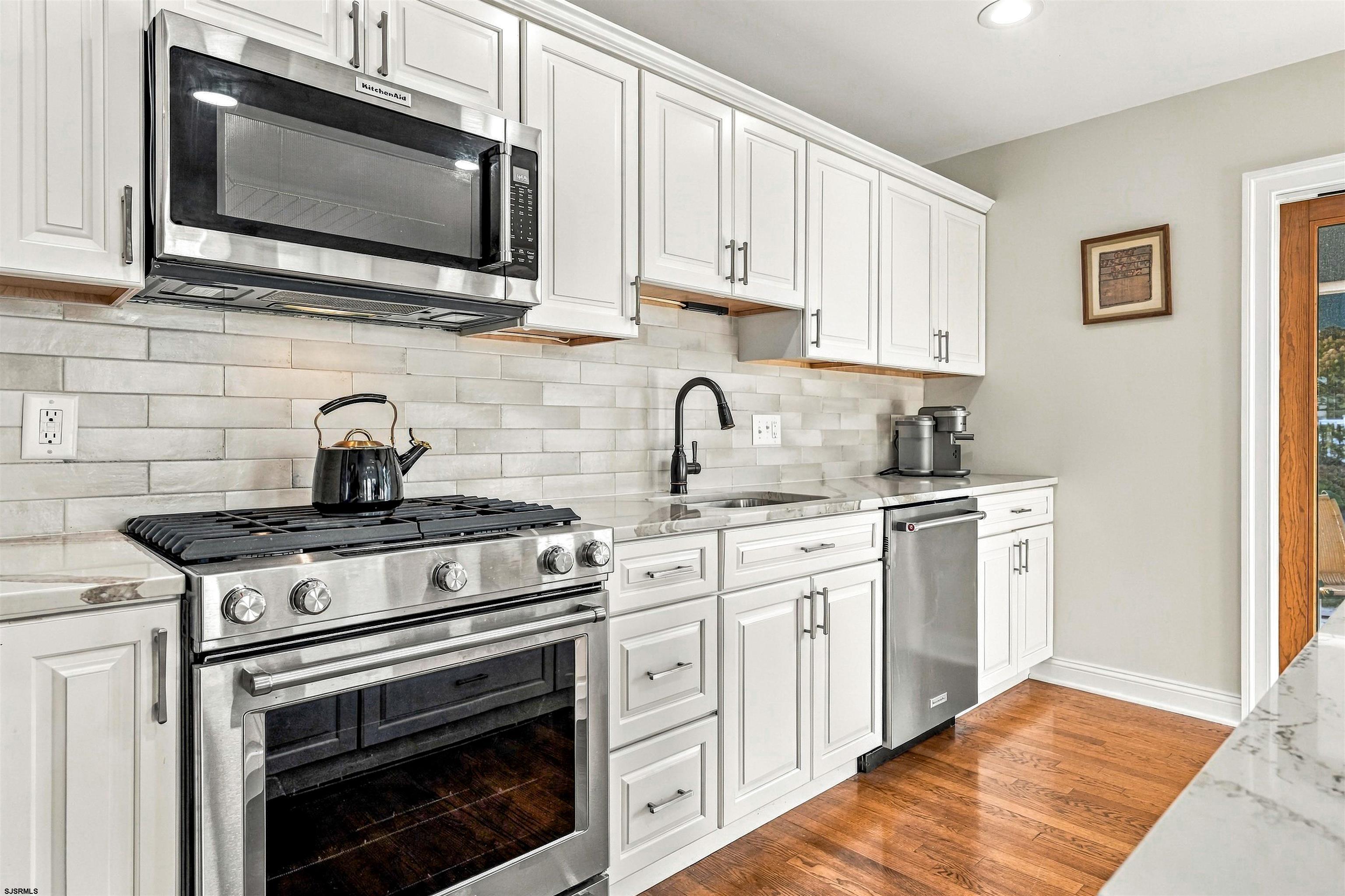 Kitchen with white cabinets, stainless appliances, a large gas range, pale tile backsplash, and wood floors.