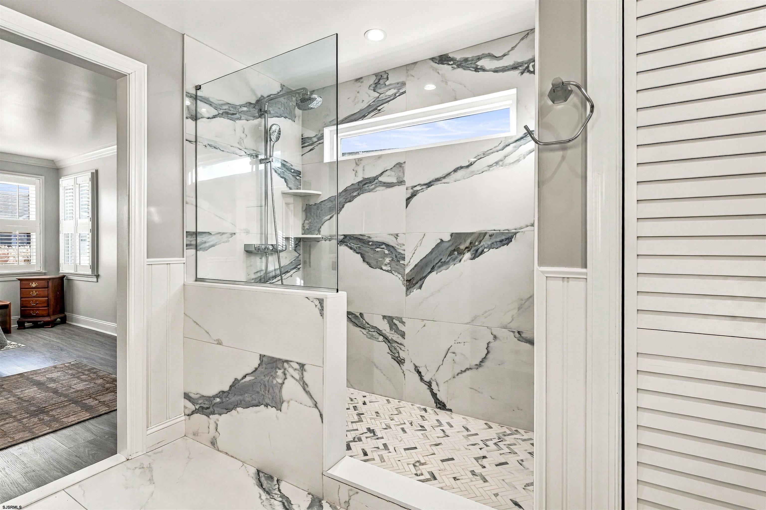 Bathroom with a glass shower, dramatic veined marble walls, and patterned tile floor.