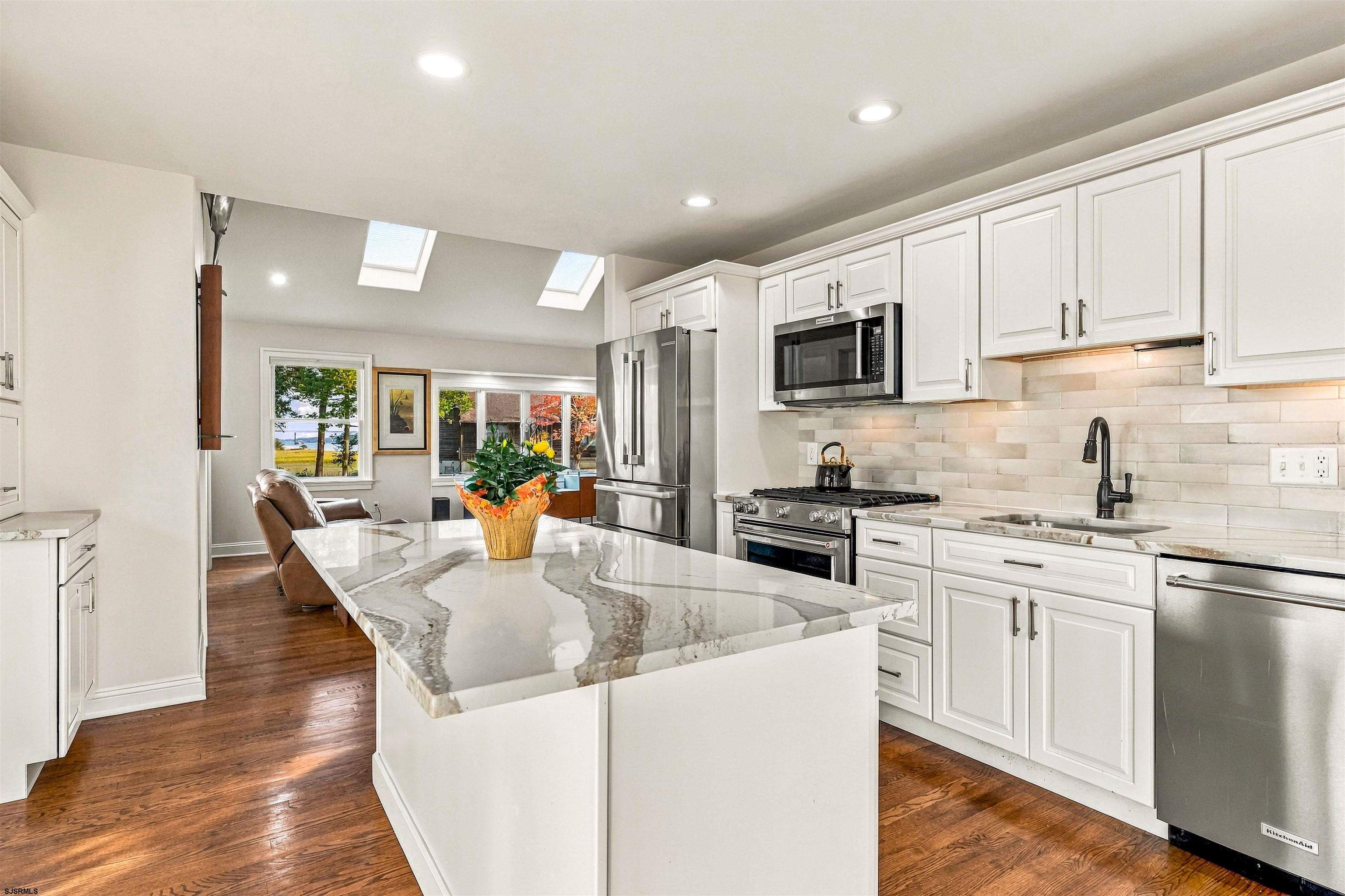 Renovated kitchen with a large veined stone island, white cabinets, and stainless steel appliances.