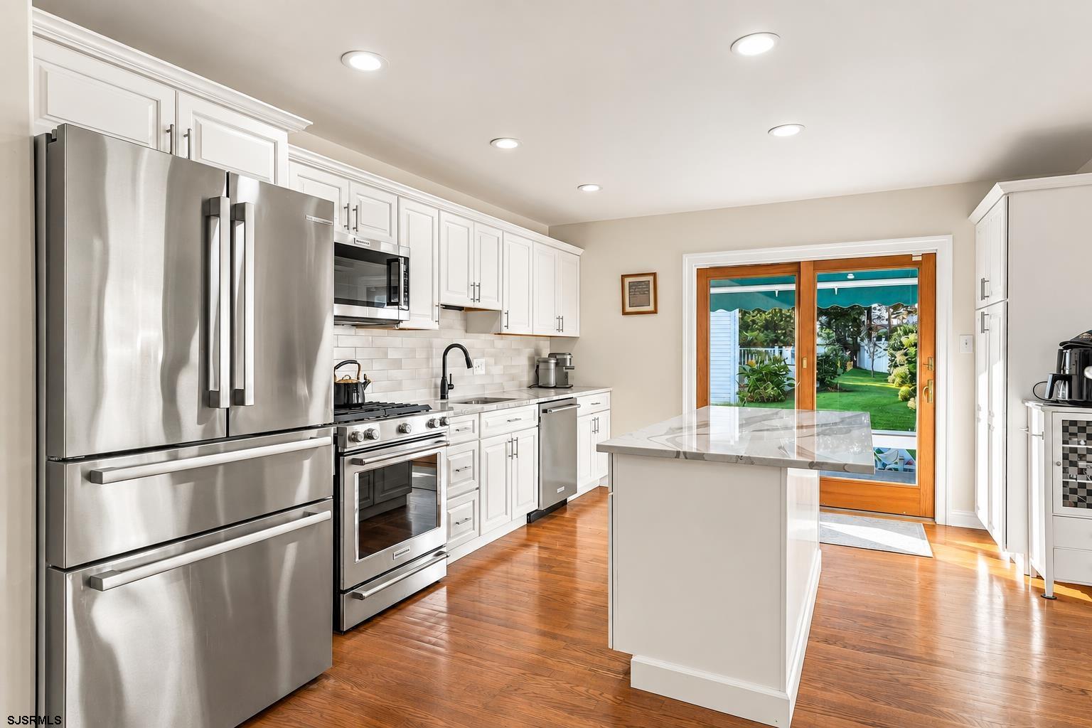 Kitchen with white cabinets, stainless steel appliances, and an island beside doors to the backyard.