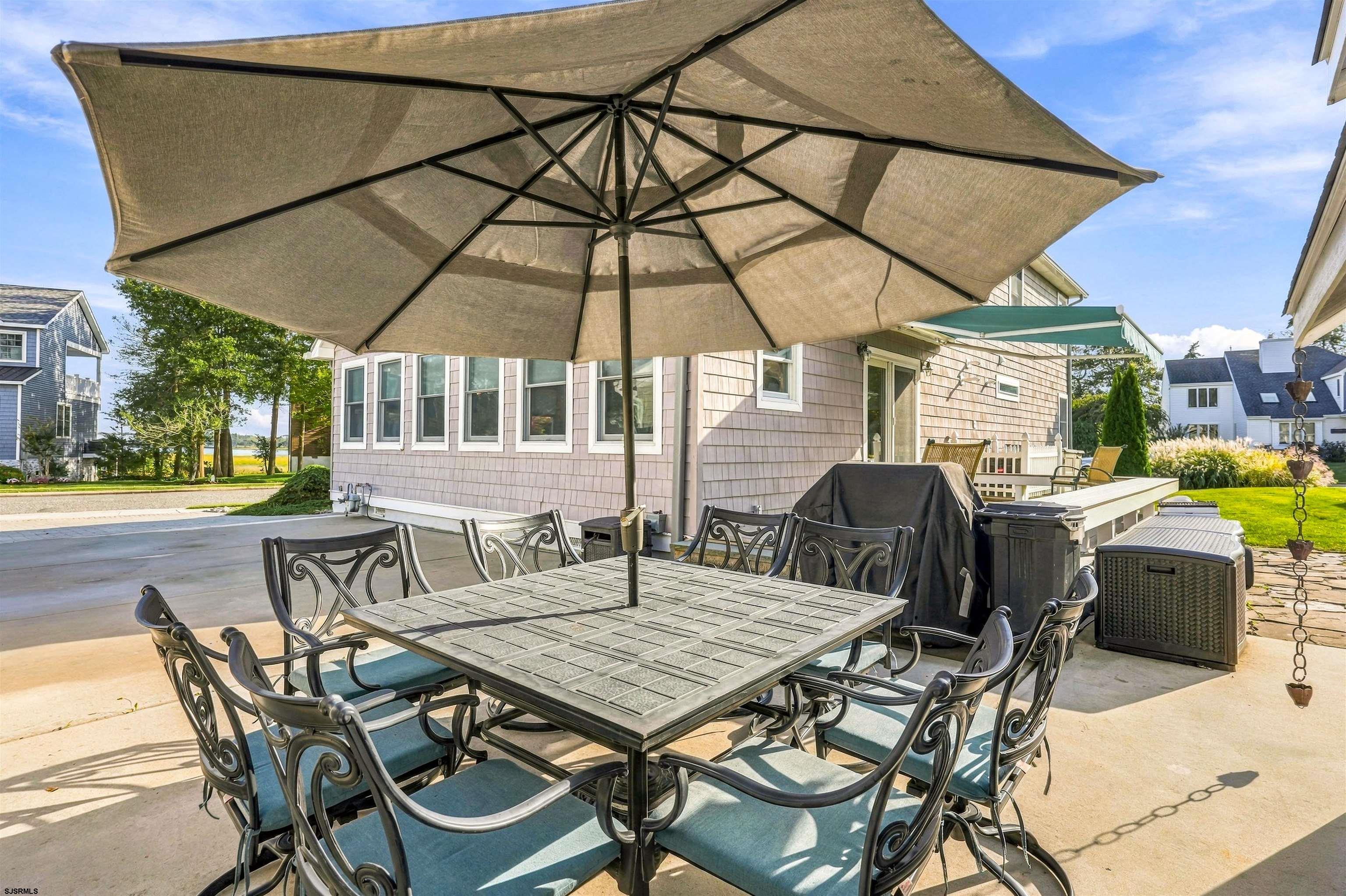 Outdoor patio with metal dining set beneath a large umbrella beside a shingle-sided home.