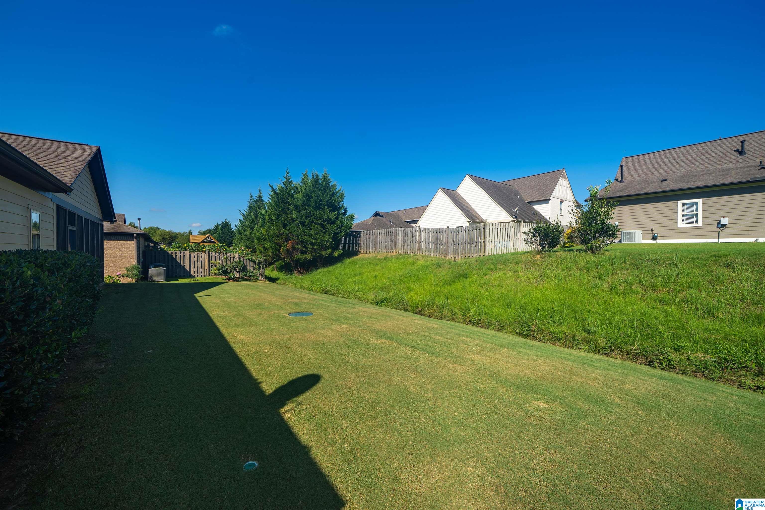 Sloping backyard lawn with a small putting green and wooden fence, viewed toward neighboring homes.