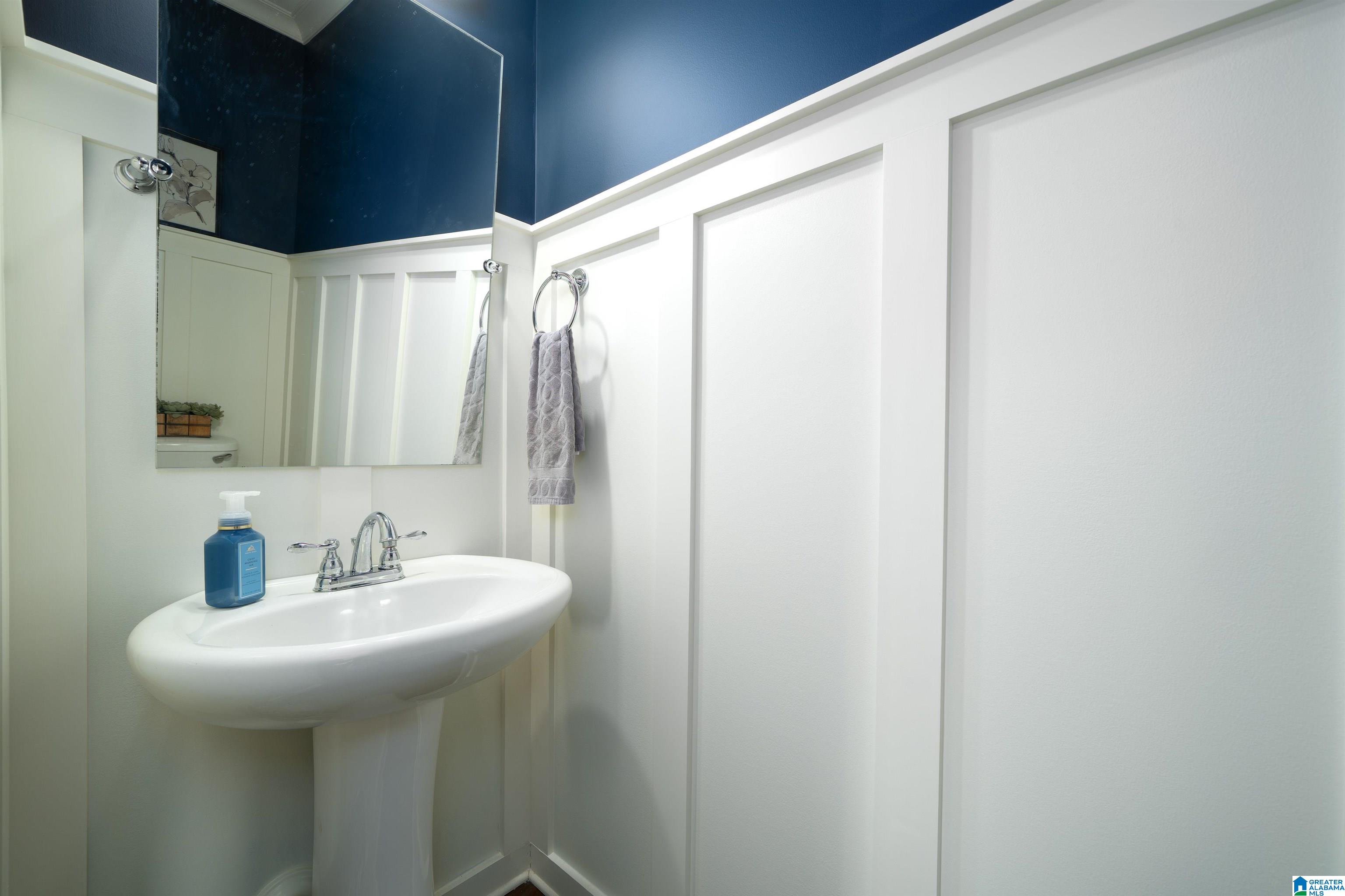 Bathroom pedestal sink with chrome faucet, mirror, gray towel, and navy blue upper walls.