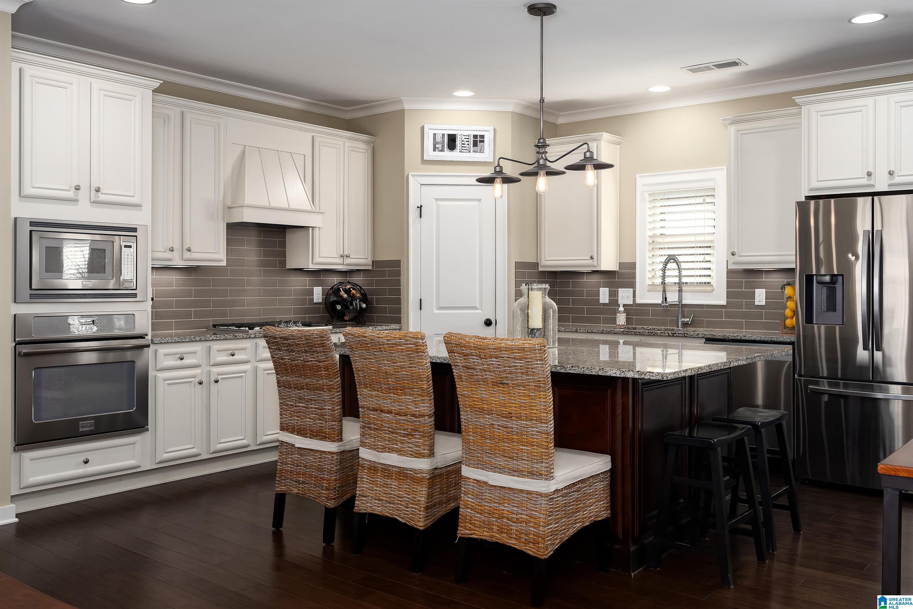 Kitchen with white cabinets, granite island, wicker stools, and stainless steel appliances.