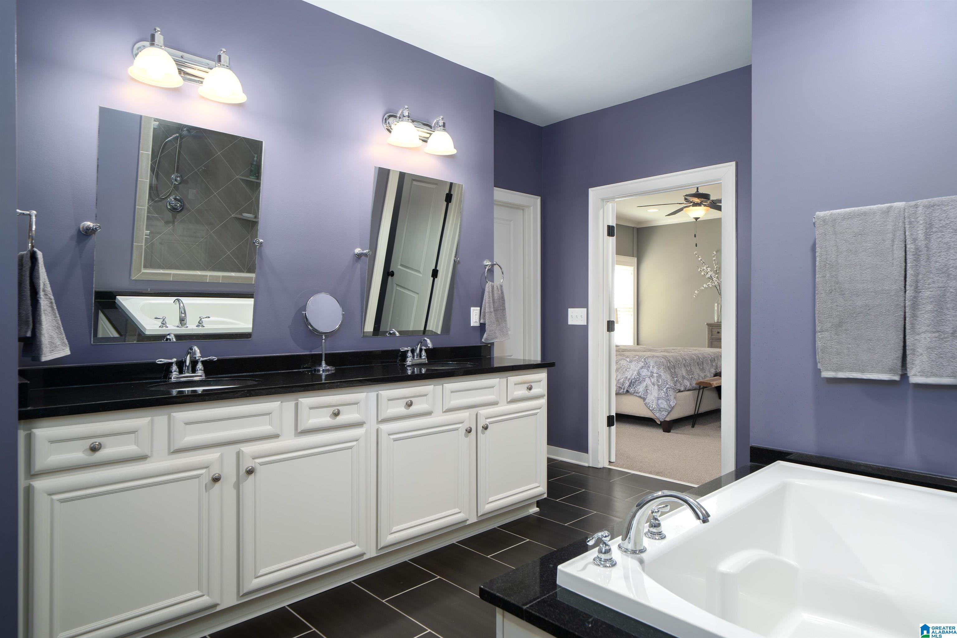Bathroom with a white double vanity and a large soaking tub beside an open bedroom doorway.
