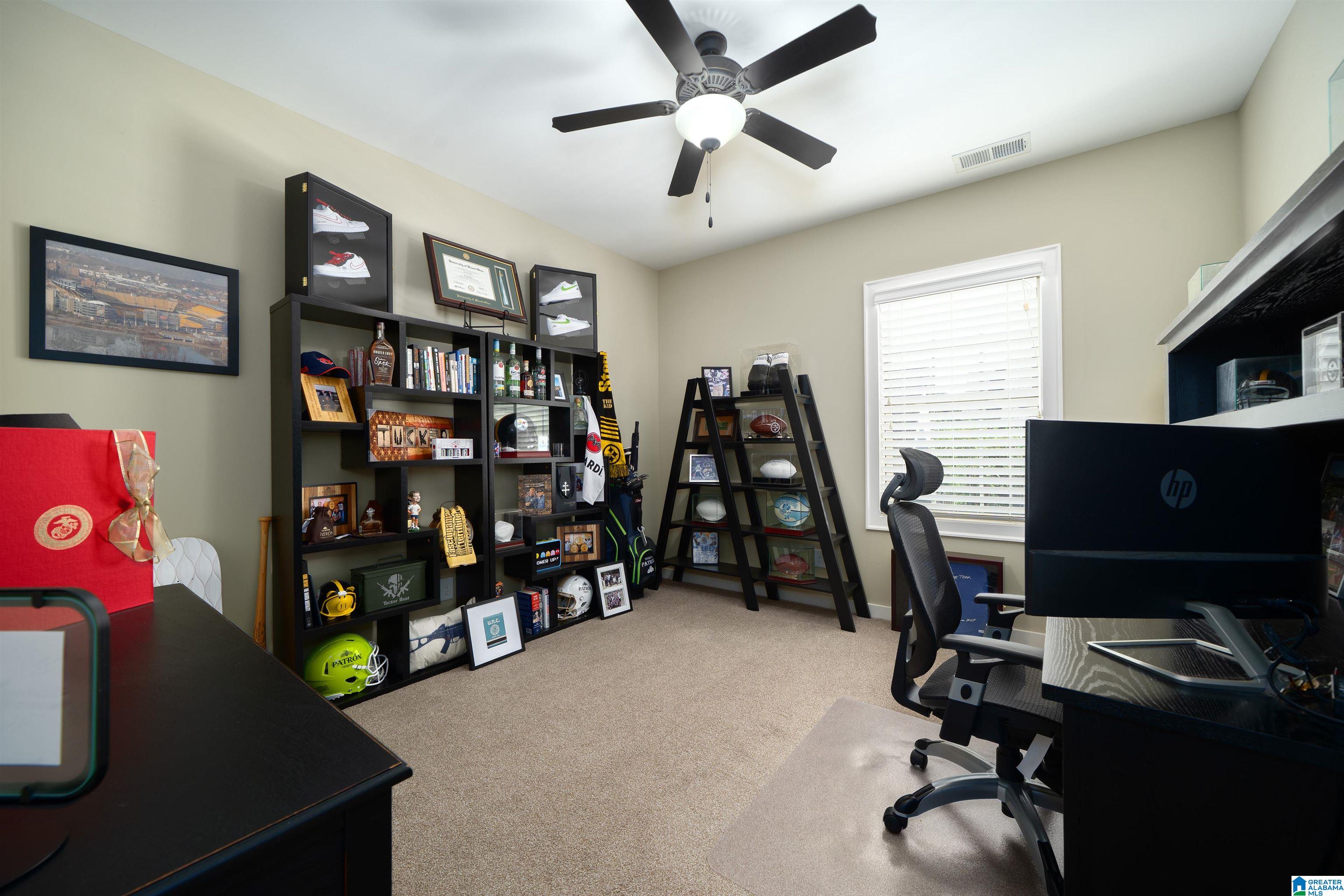 Home office with sports memorabilia-filled shelves, a computer desk, and a window with white blinds.