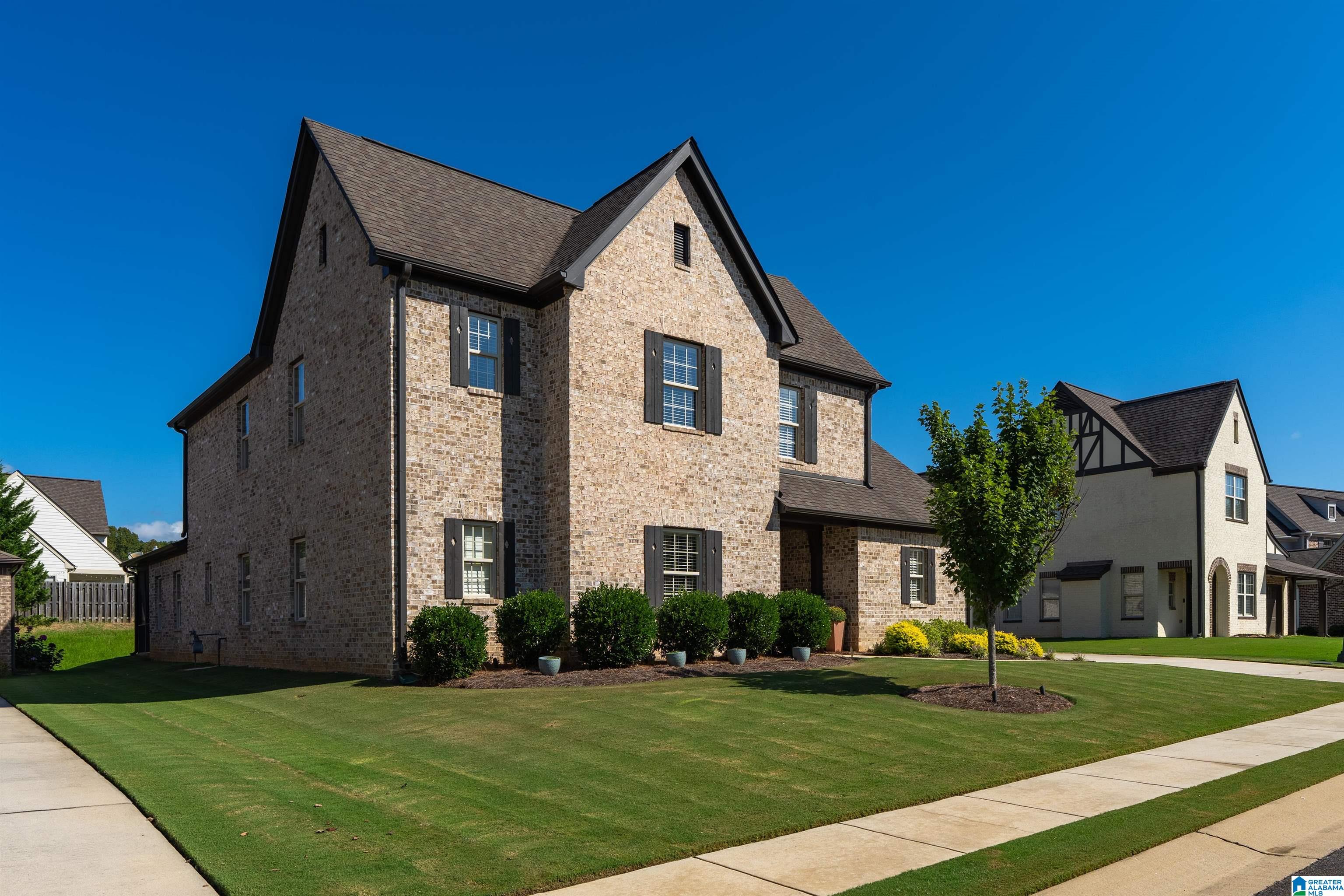 Two-story brick house with dark shutters, trimmed shrubs, and a broad lawn.