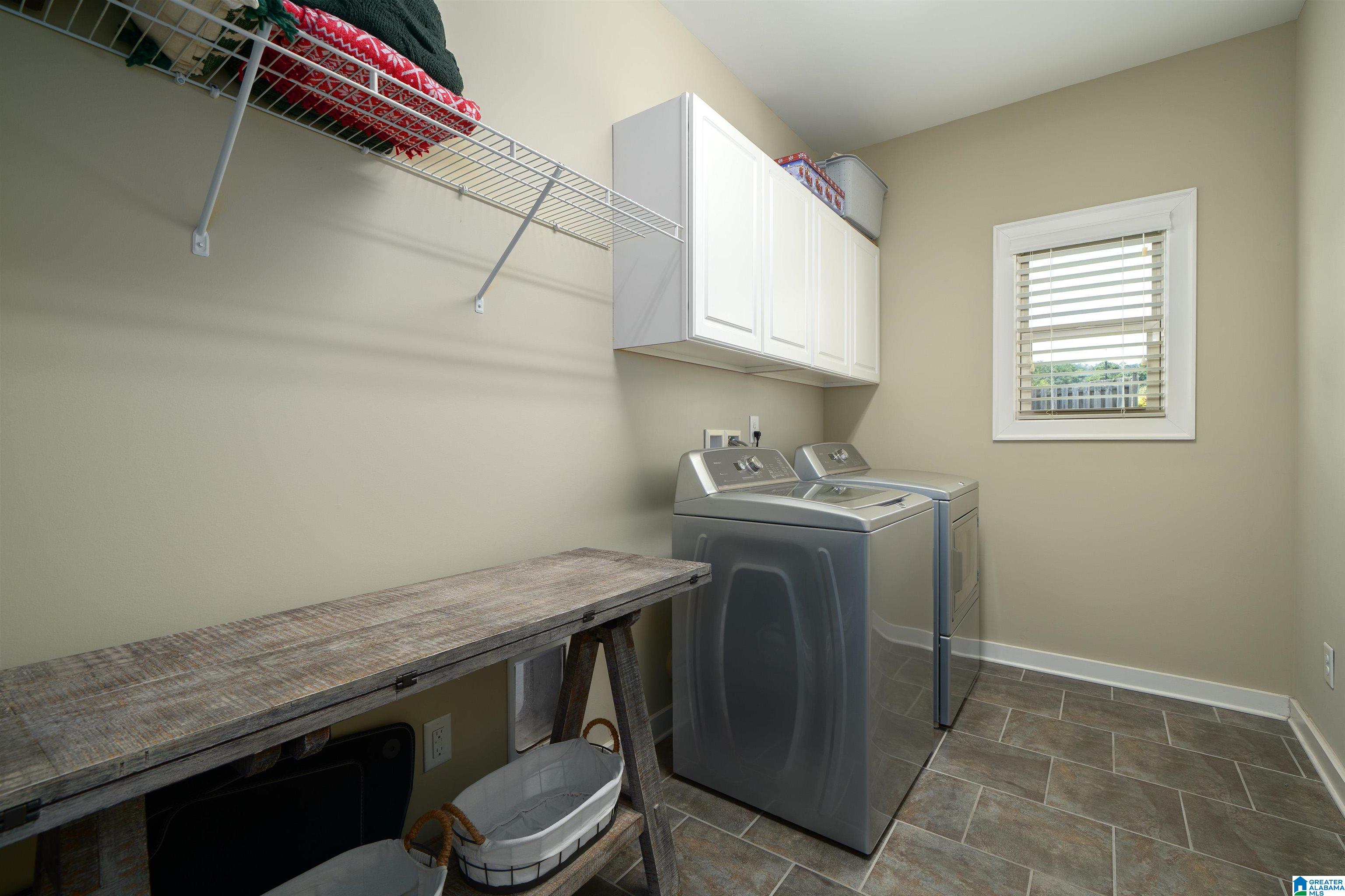 Laundry room with washer and dryer, white cabinets, wire shelving, and a rustic wooden worktable.