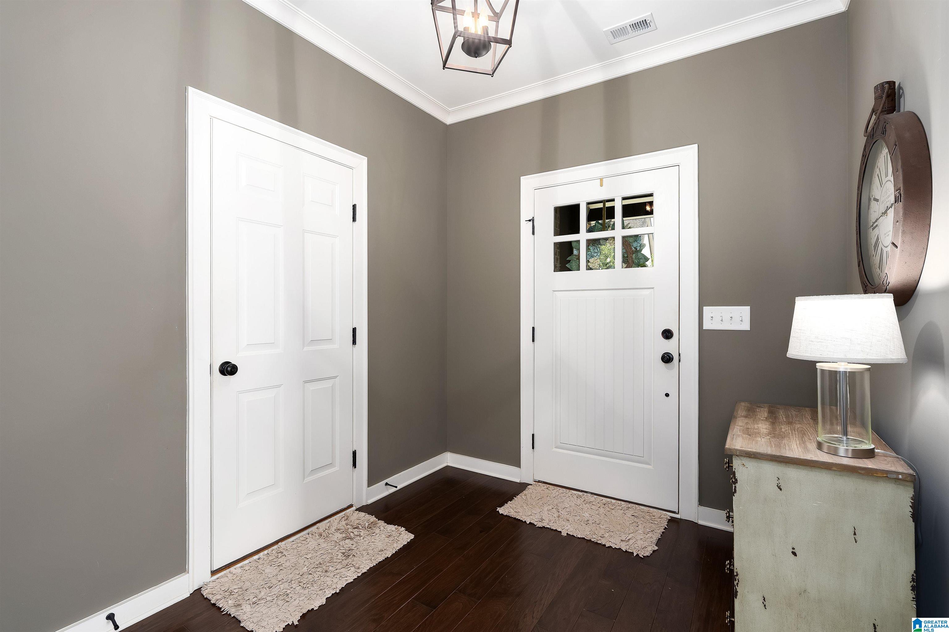 Entry foyer with a glass-paneled white front door, dark wood floors, and a distressed console cabinet.