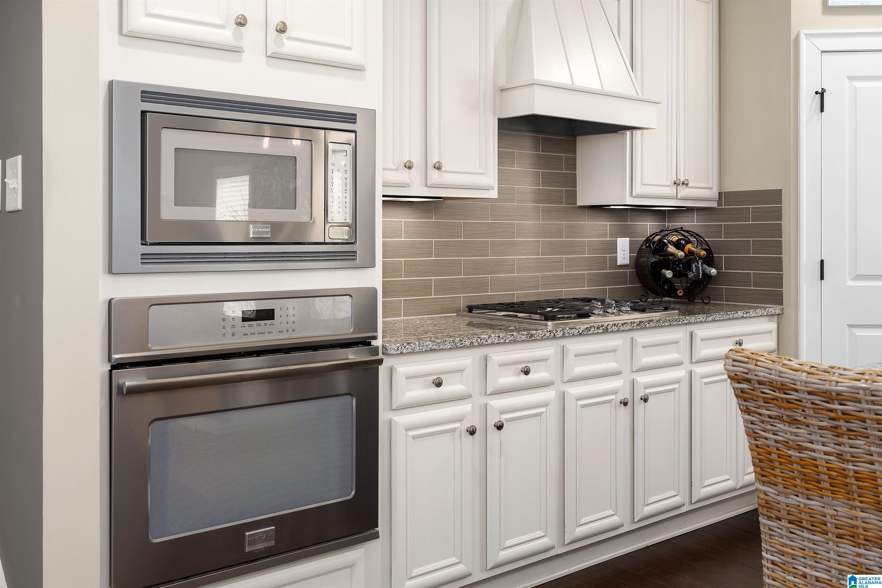 Kitchen with white cabinetry, stainless built-in appliances, gas cooktop, and taupe tile backsplash.
