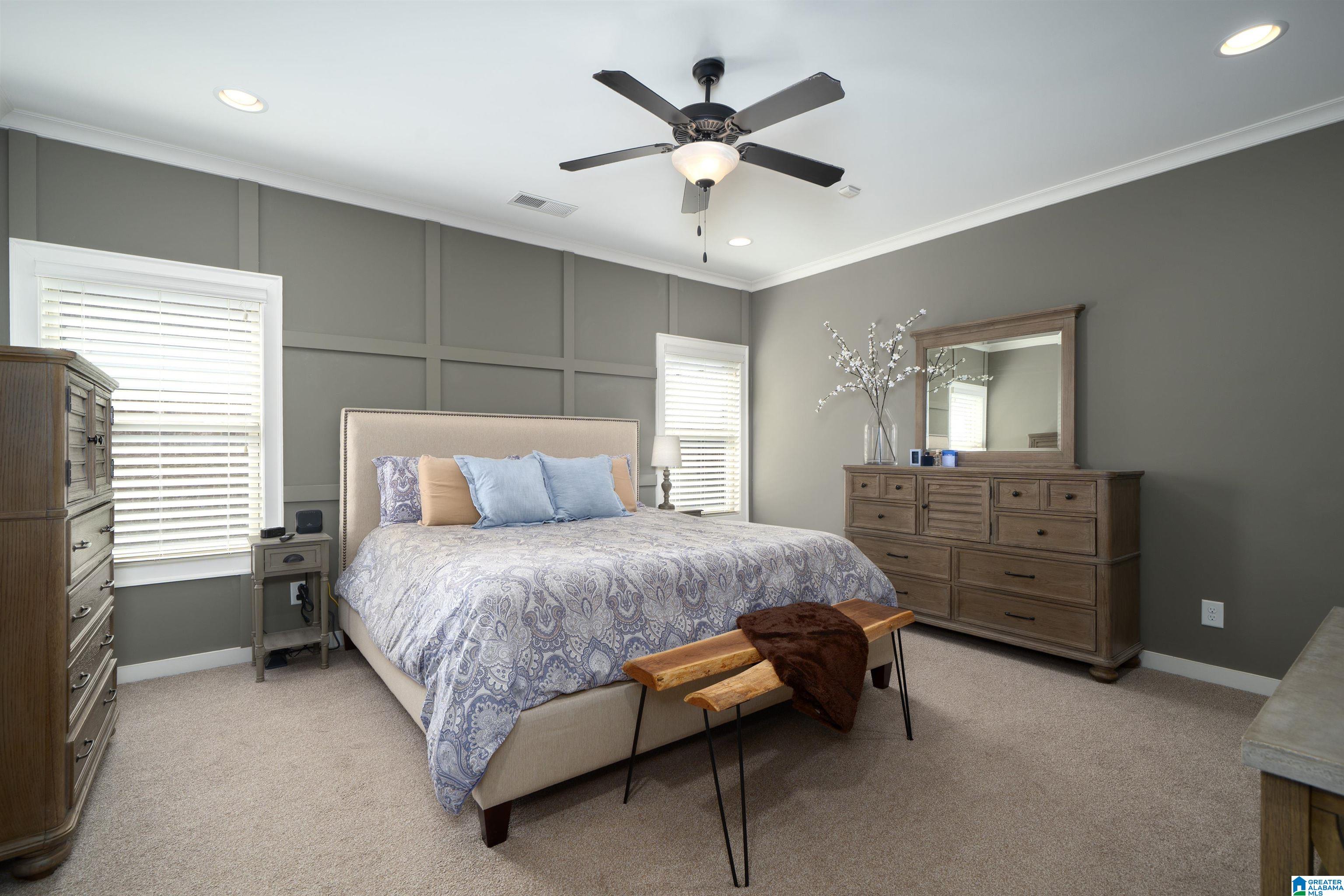 Furnished bedroom with a patterned bed, wooden dresser and mirror, and ceiling fan.