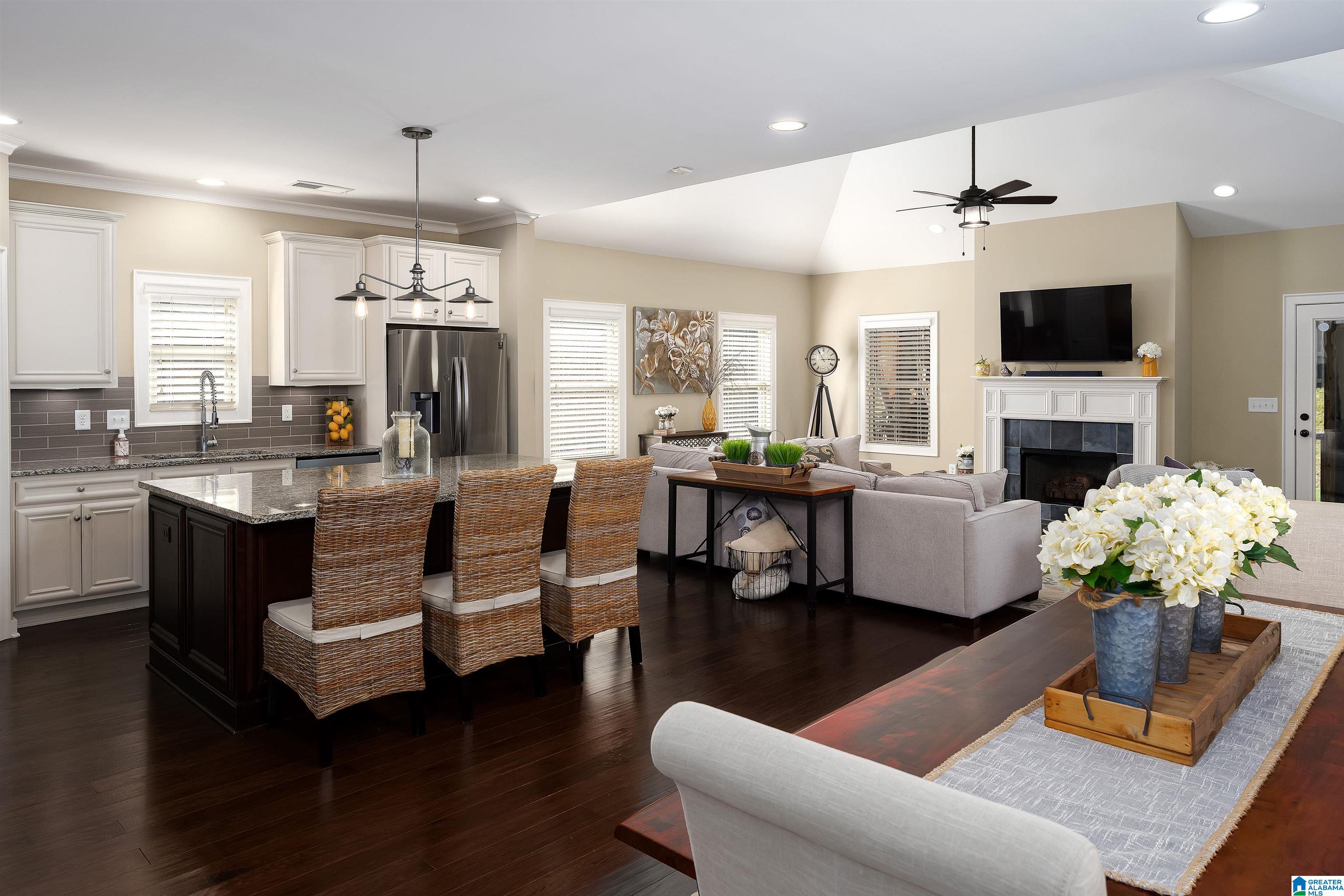 Open-plan kitchen and living room with a dark island, woven barstools, and fireplace.