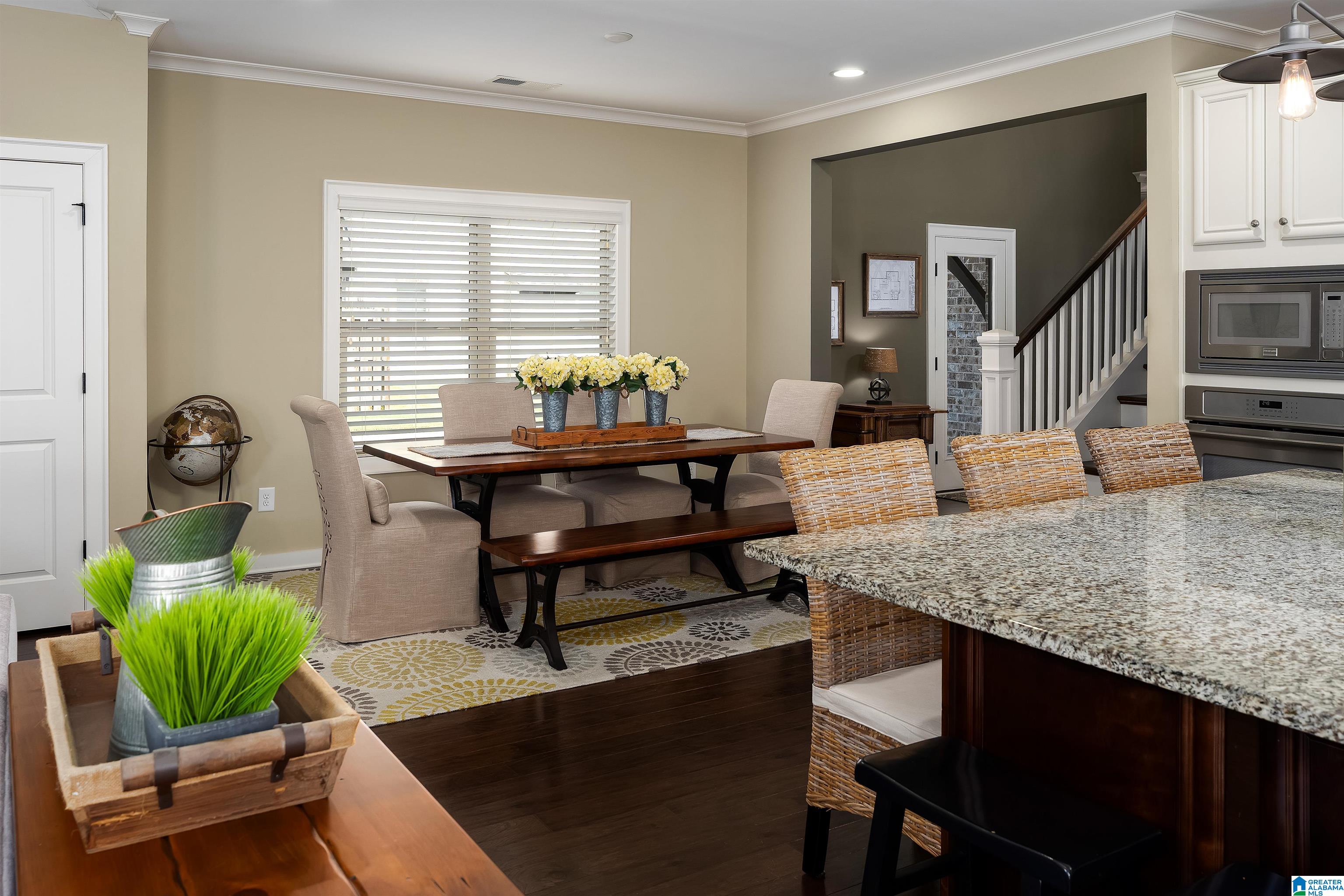 Dining area with a dark wood table beside a granite kitchen island and staircase.