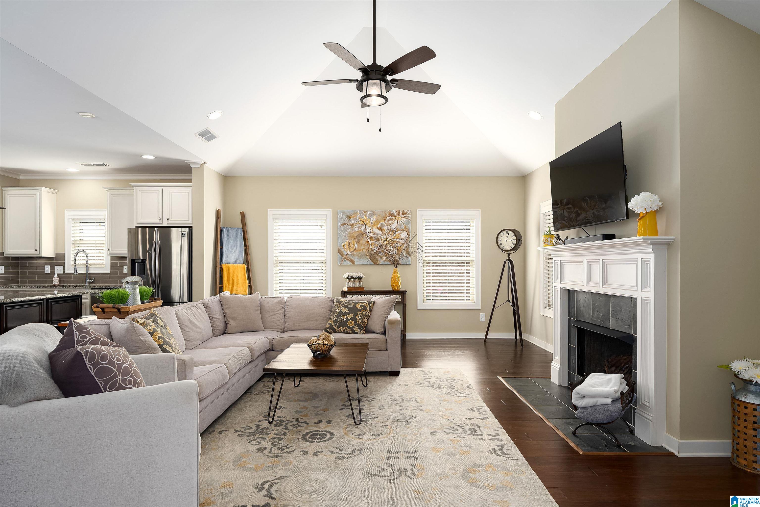 Furnished living room with a vaulted ceiling, sectional sofa, and white fireplace beneath a mounted television.