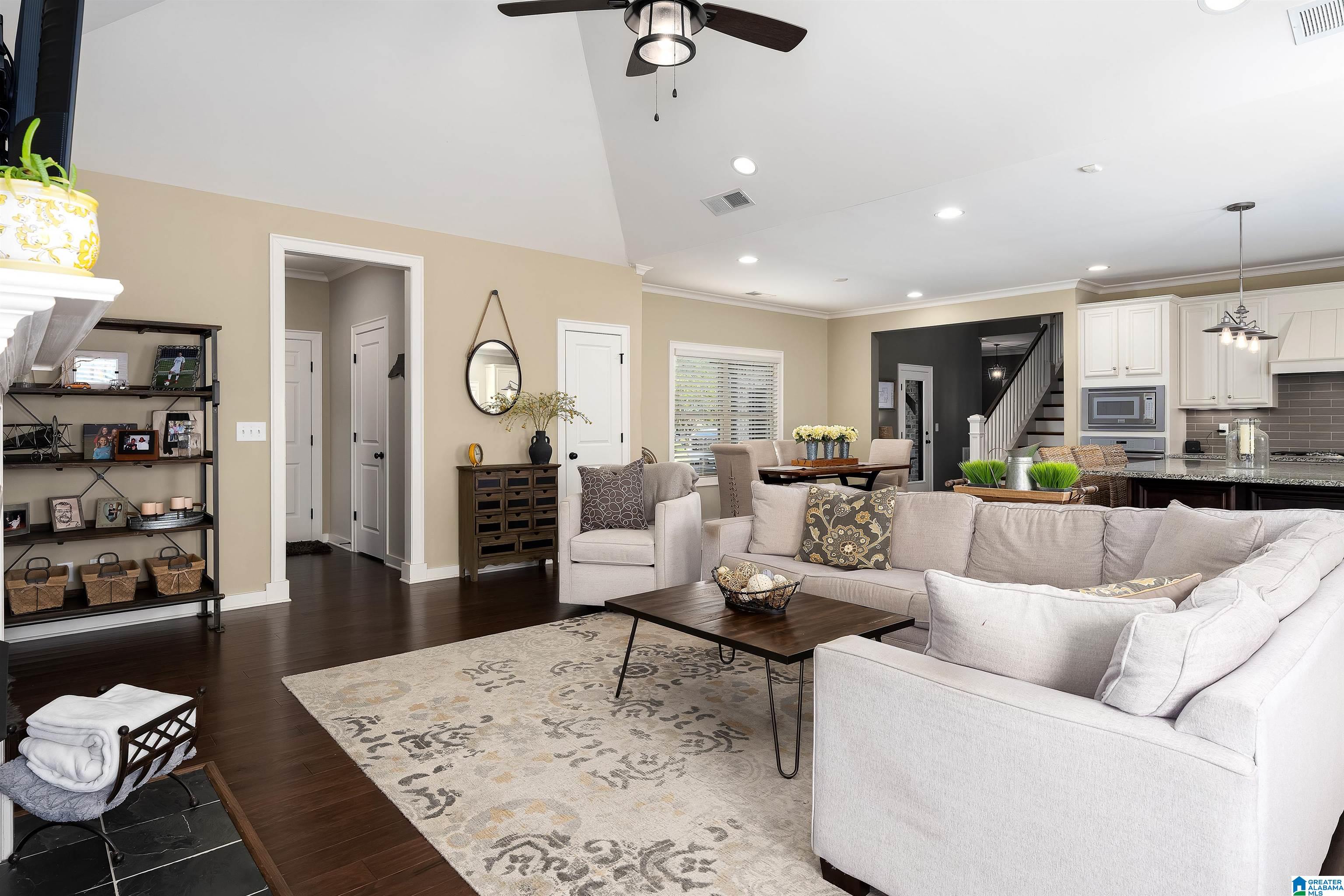 Open-plan living room with a large white sectional, dark wood floors, and the dining area and kitchen beyond.