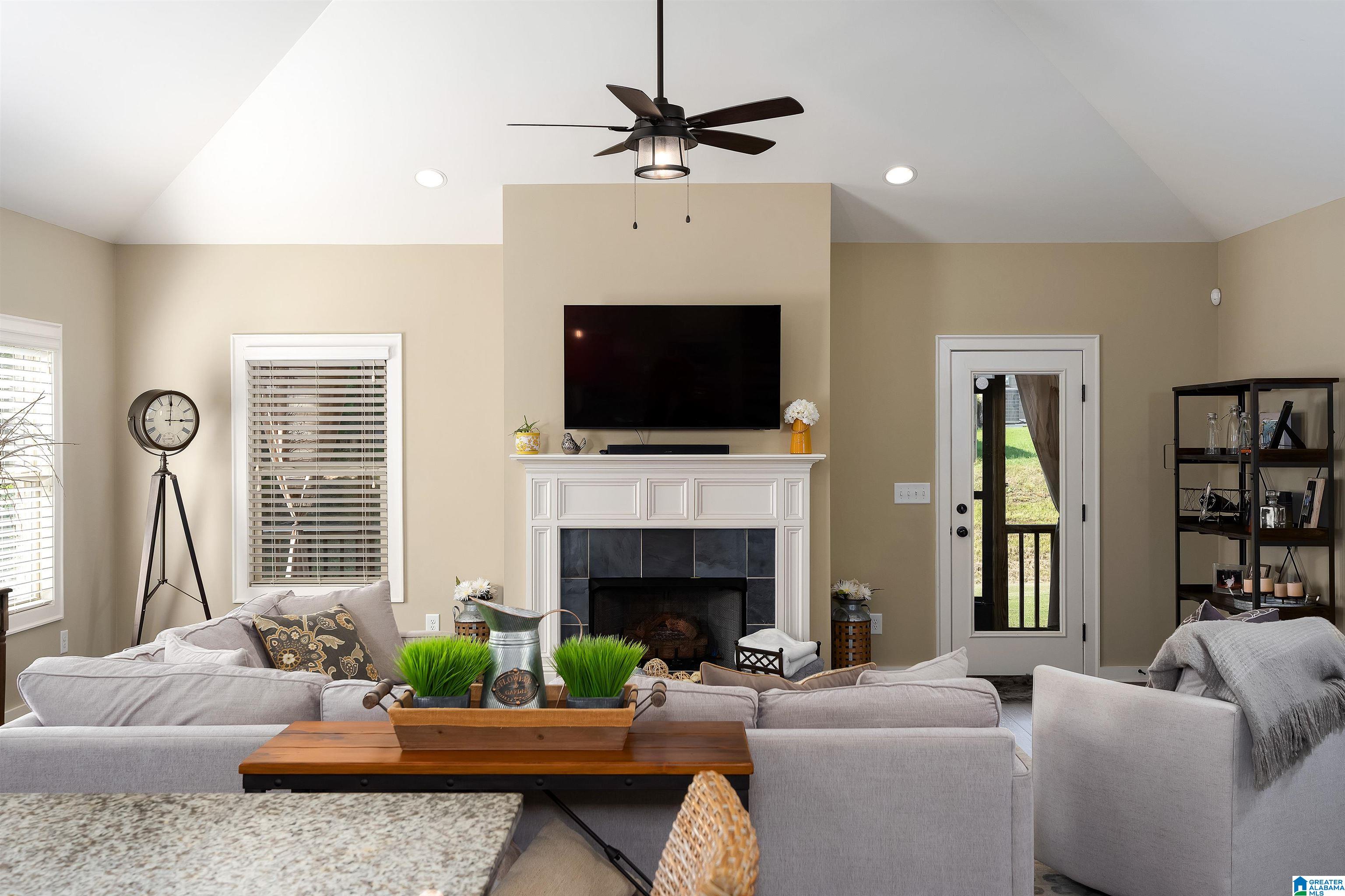 Furnished living room with a vaulted ceiling, white fireplace, mounted television, and gray sofas.