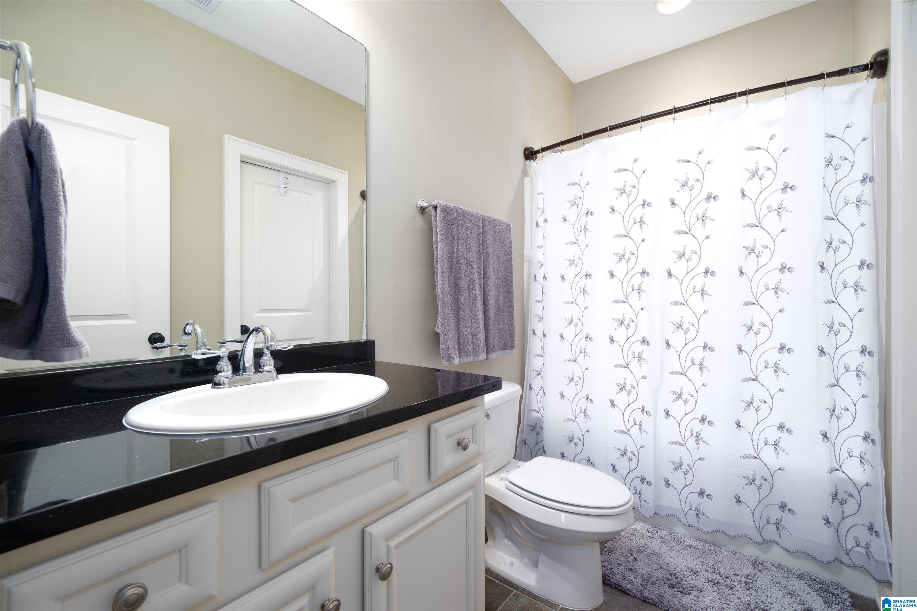 Bathroom with a black countertop vanity, white sink, toilet, and floral shower curtain.