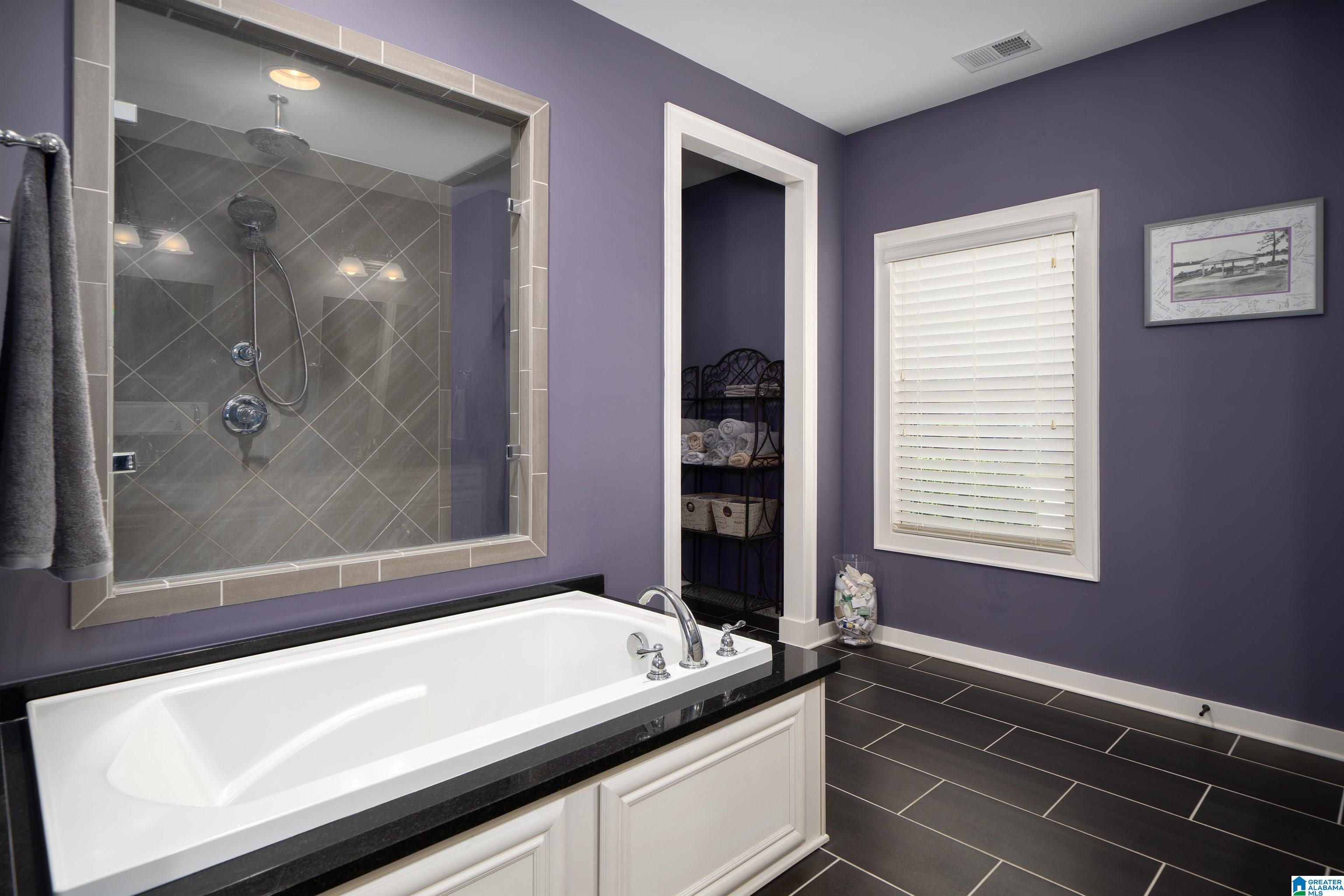Bathroom with a white jetted soaking tub and a glass-enclosed gray tiled shower.