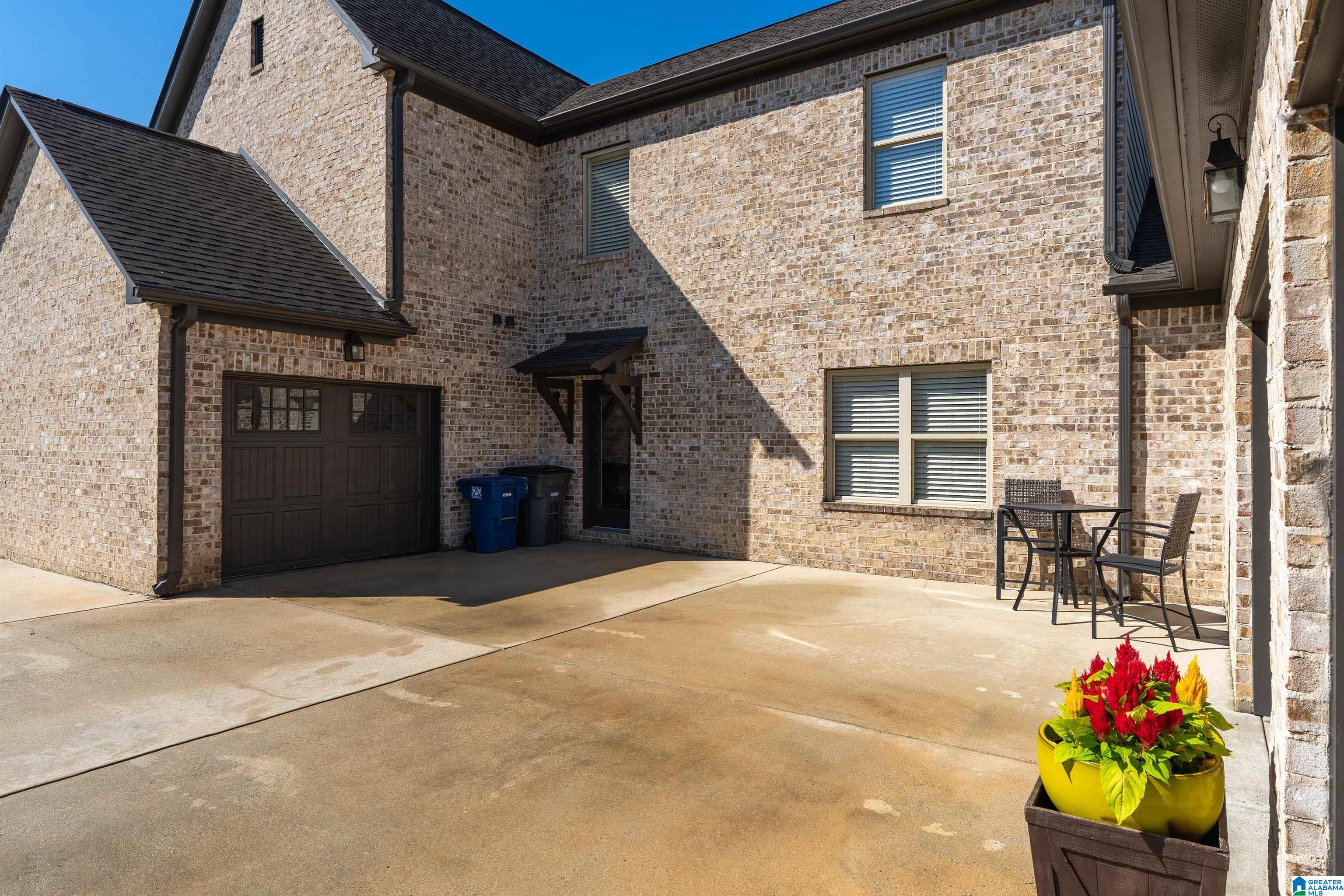 Two-story brick home with a driveway, dark garage door, and a small patio seating area.