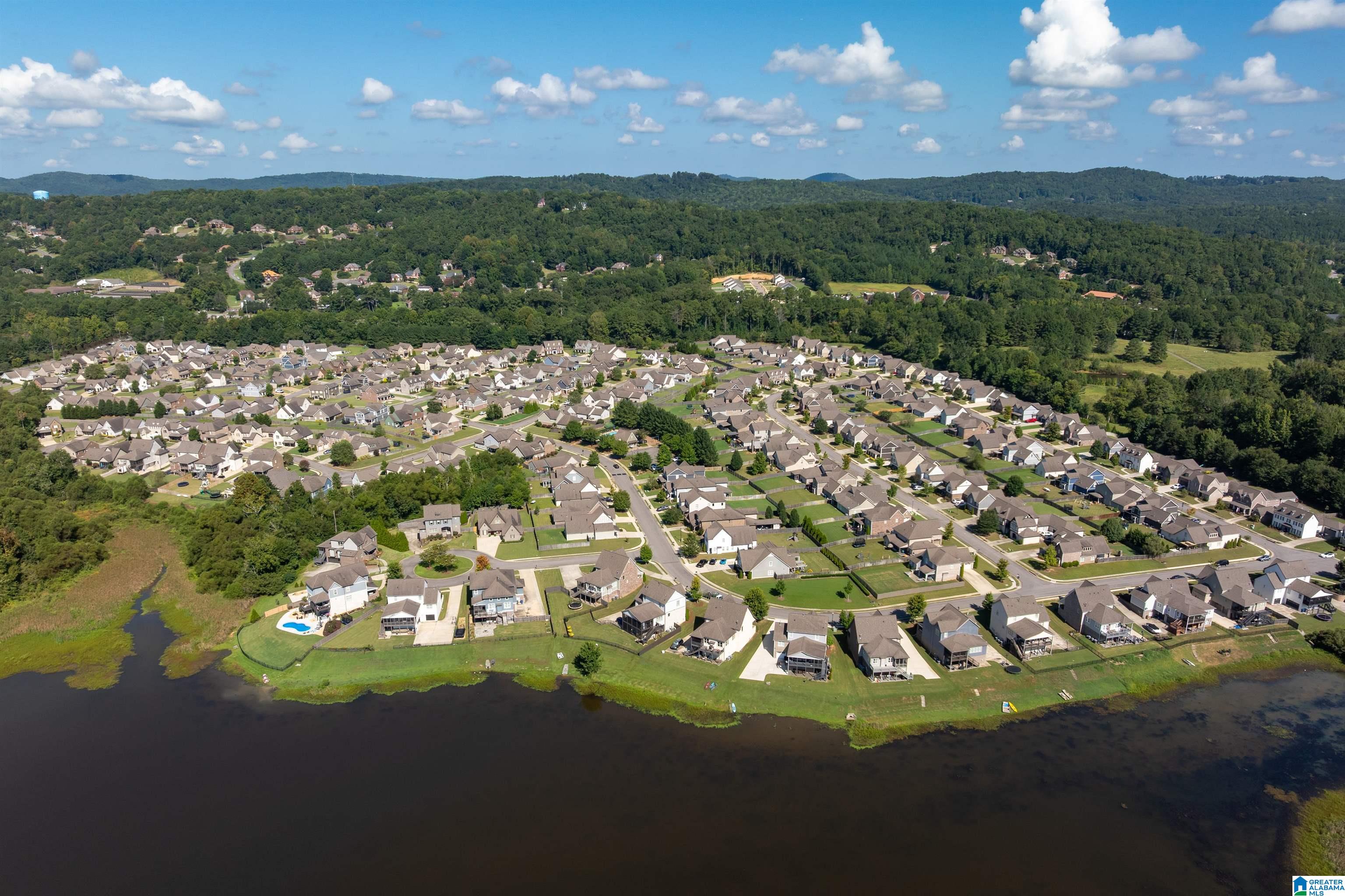 Aerial view of a waterfront neighborhood with rows of homes and wooded hills beyond.