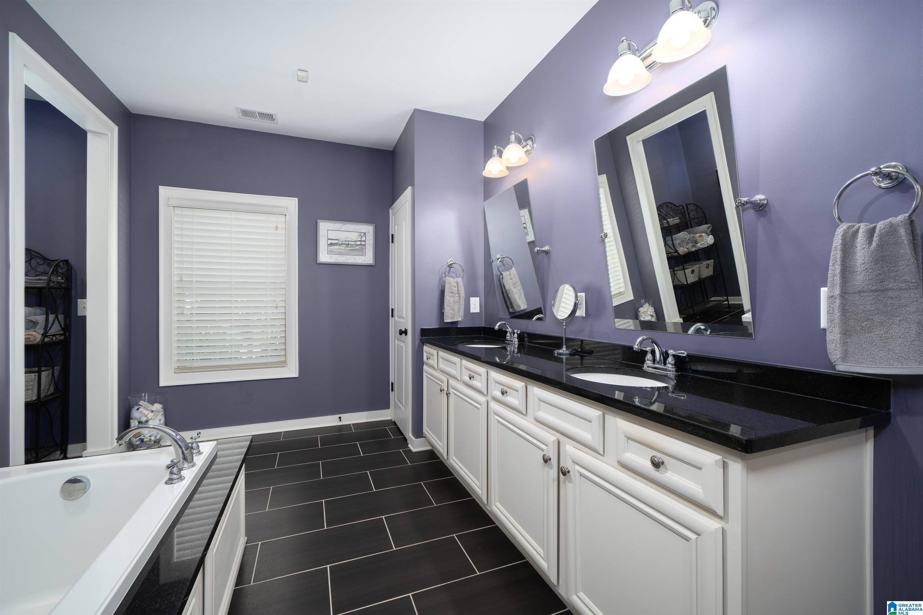 Bathroom with a long double vanity, black countertop, purple walls, and a white bathtub.