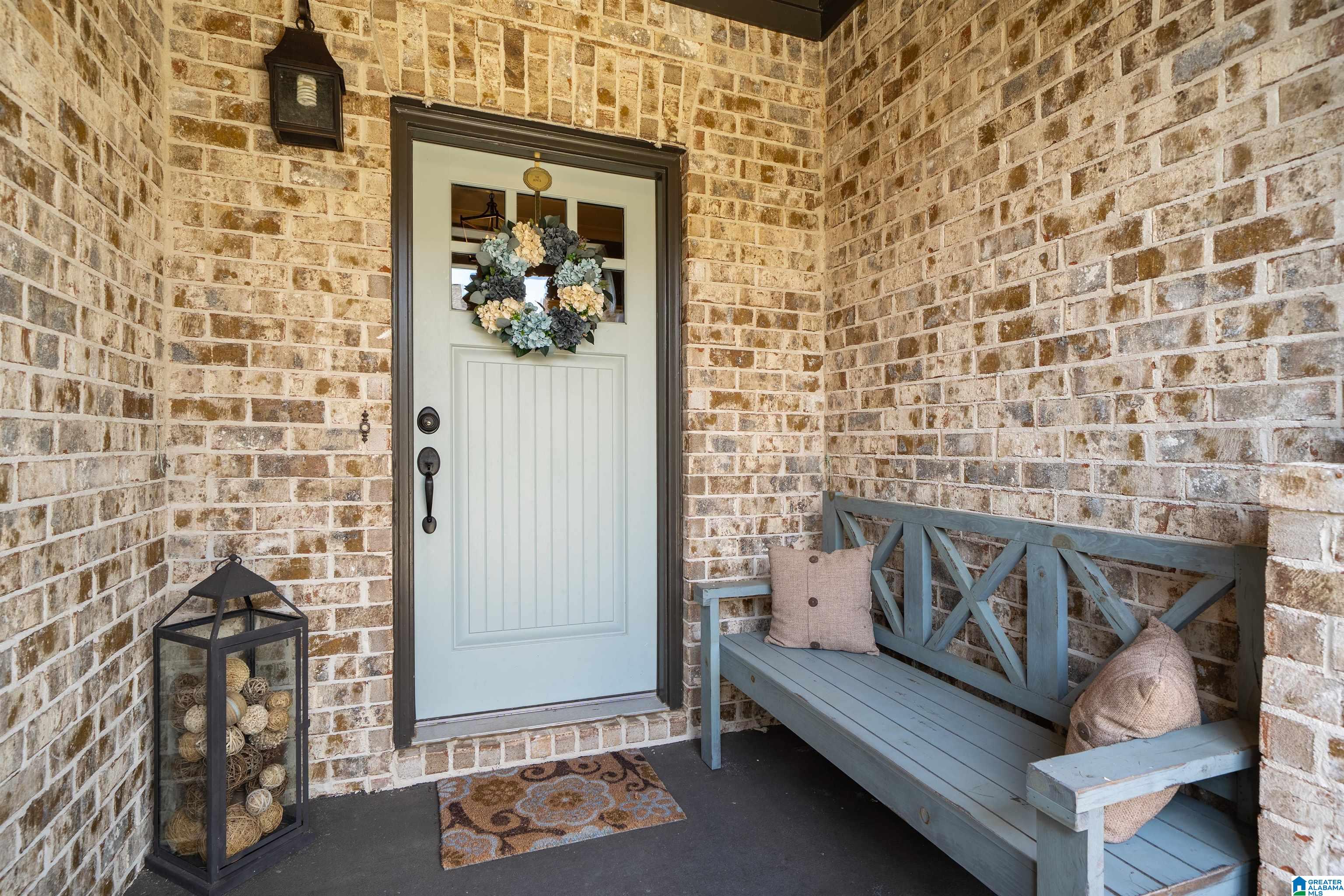 Front porch with a white door and wreath, brick walls, and a blue-gray bench.