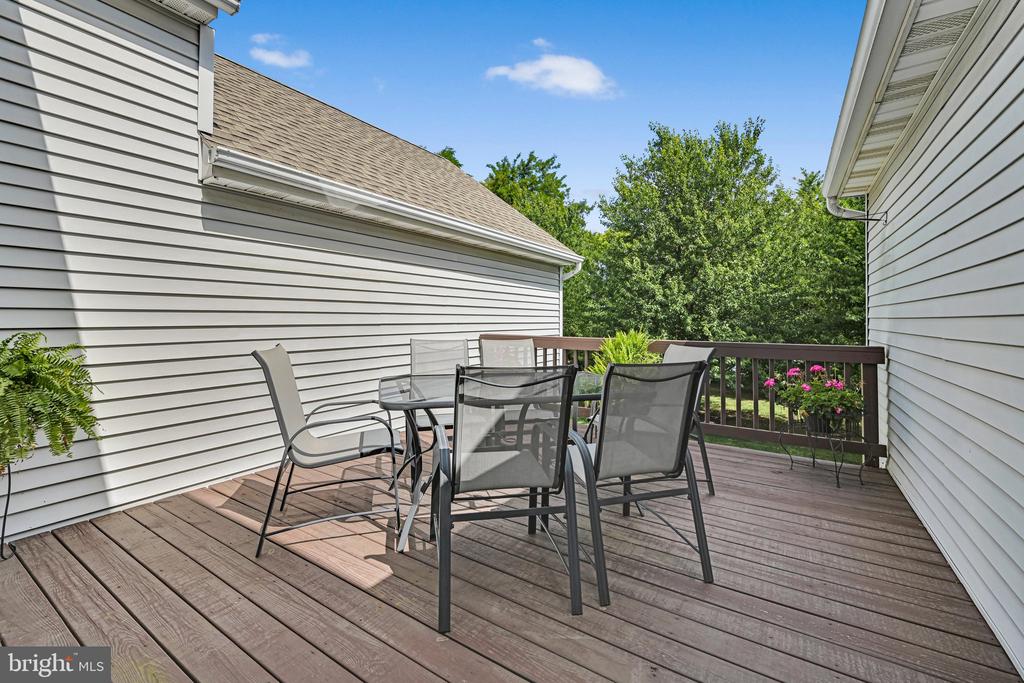 Wooden deck with a black metal dining set and trees beyond the railing.