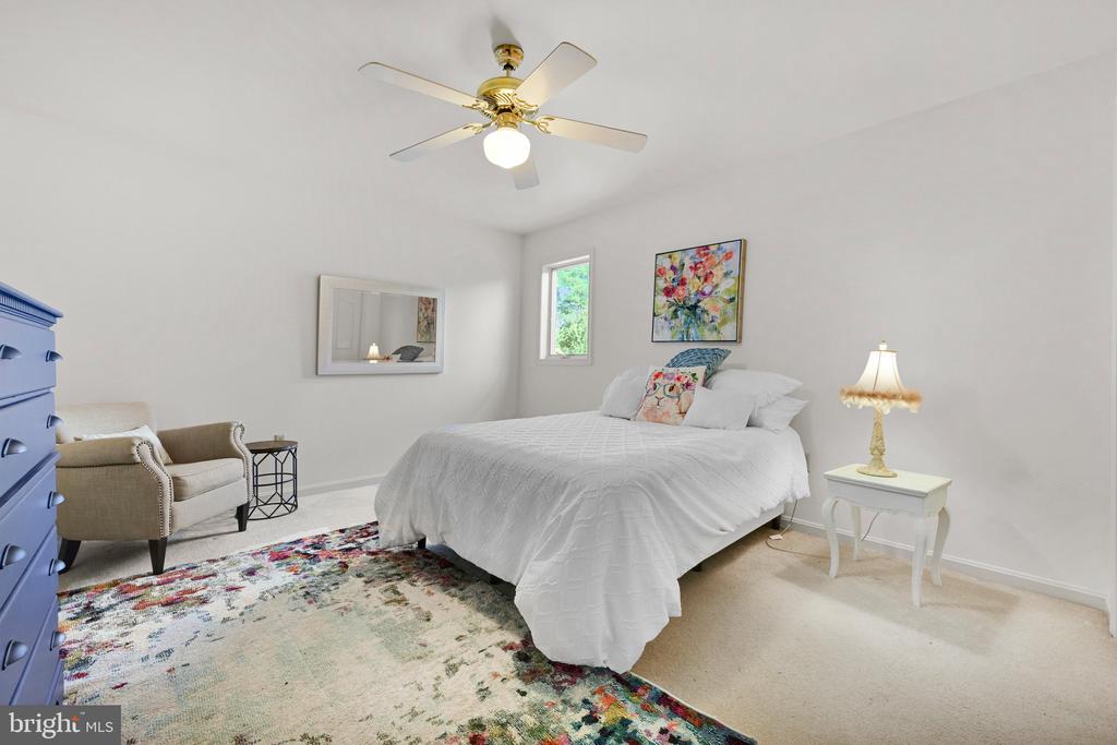 Bedroom with a white bed, colorful floral rug, blue dresser, and beige armchair.