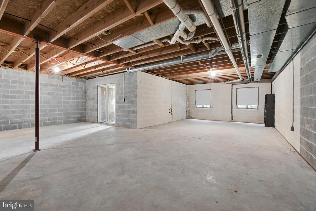 Unfinished basement with exposed ceiling joists and HVAC ducts, concrete floor, and gray block walls.