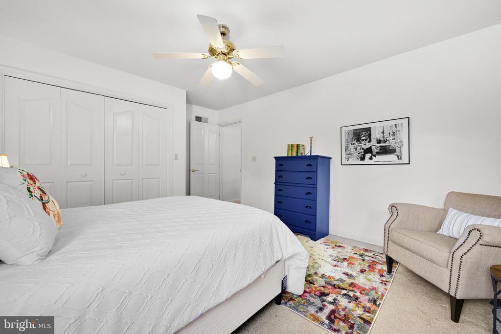 Bedroom with a white bed, blue dresser, colorful rug, and beige armchair.