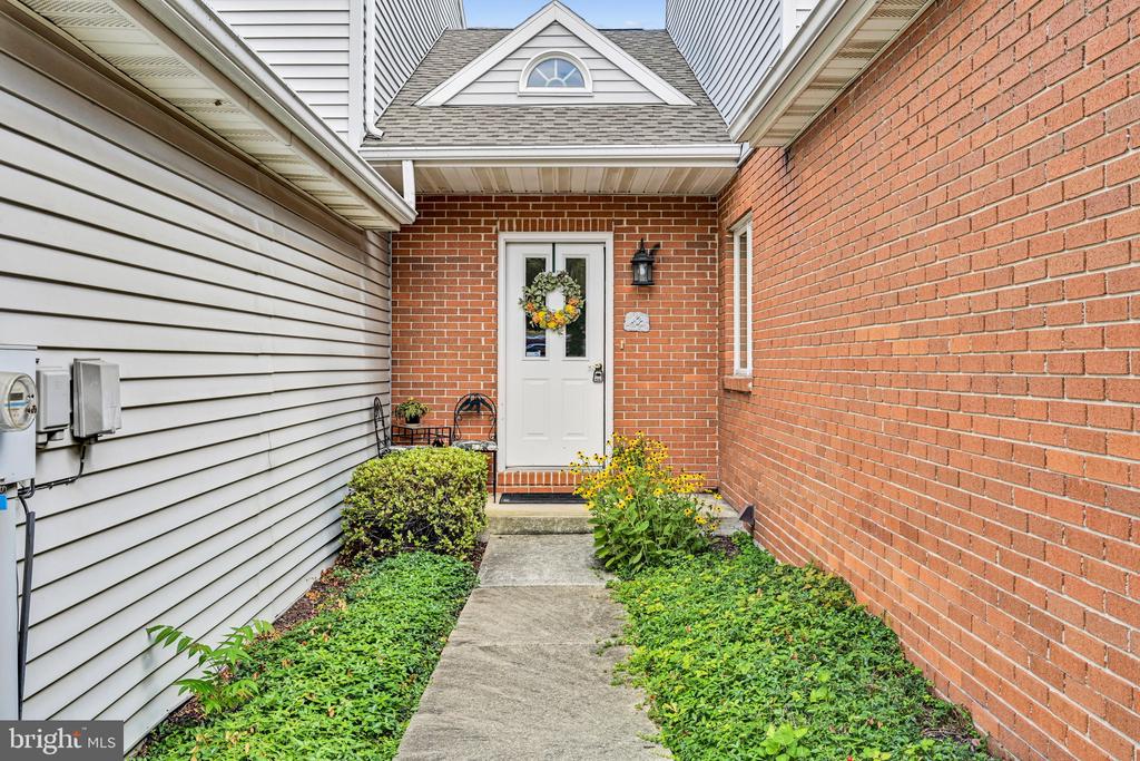 Brick home entrance with a wreath on the white door and a garden-lined concrete walkway.