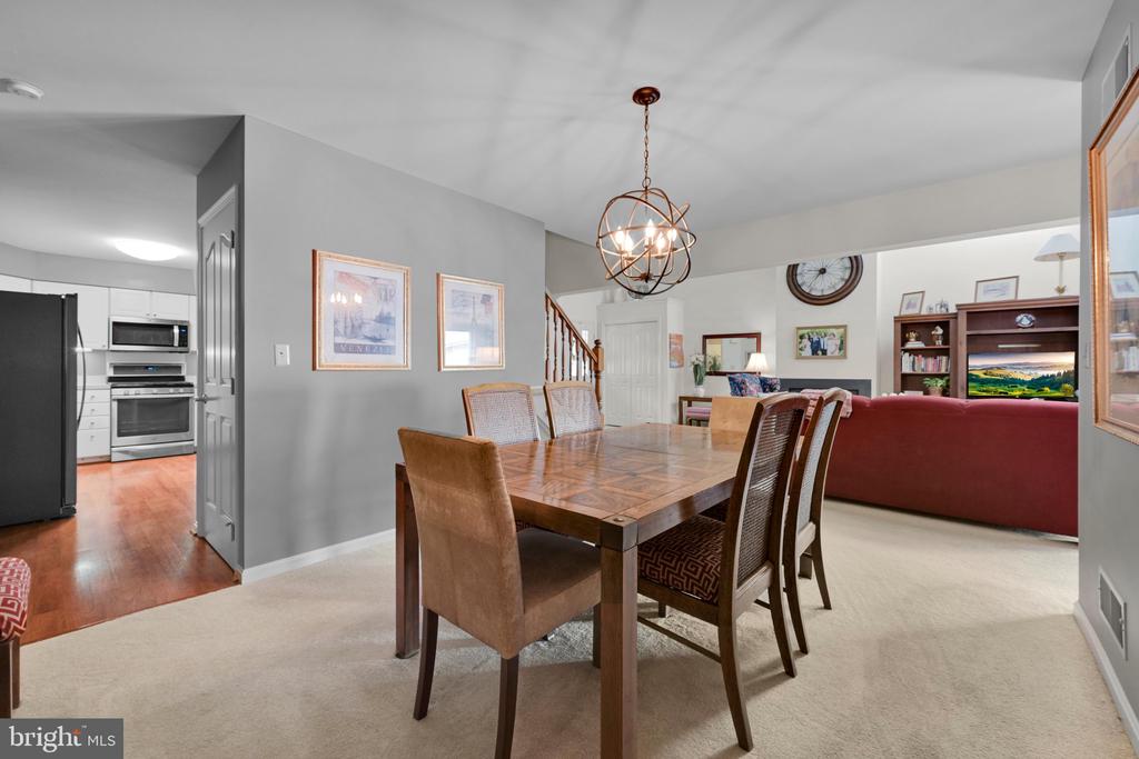 Dining room with a wooden table and sculptural pendant, opening to the kitchen and living area.