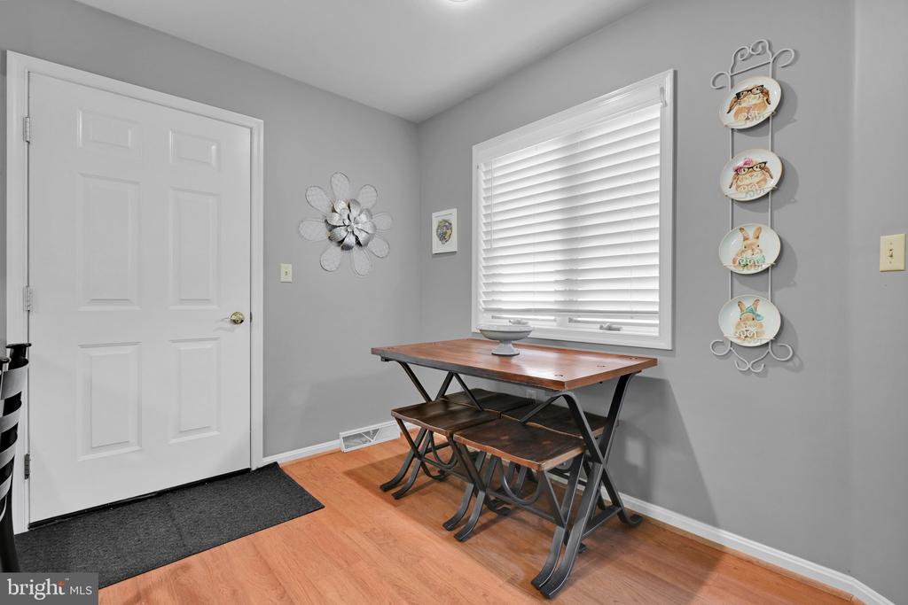 Furnished nook with a wooden table and chairs beside a bright window and white entry door.