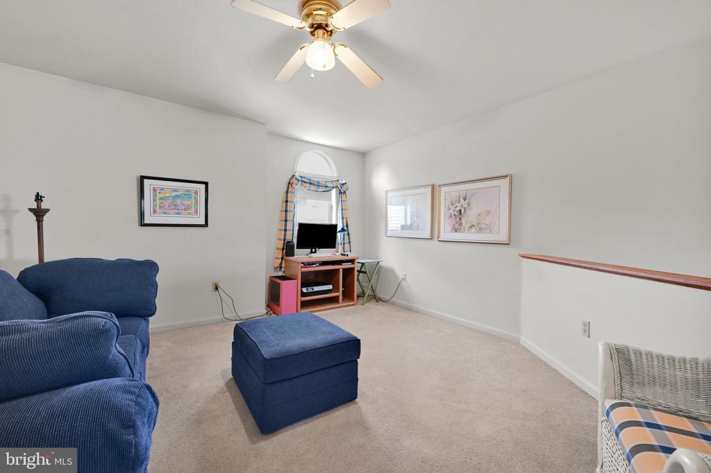 Furnished living room with a blue sofa and ottoman, TV under an arched window, and ceiling fan.