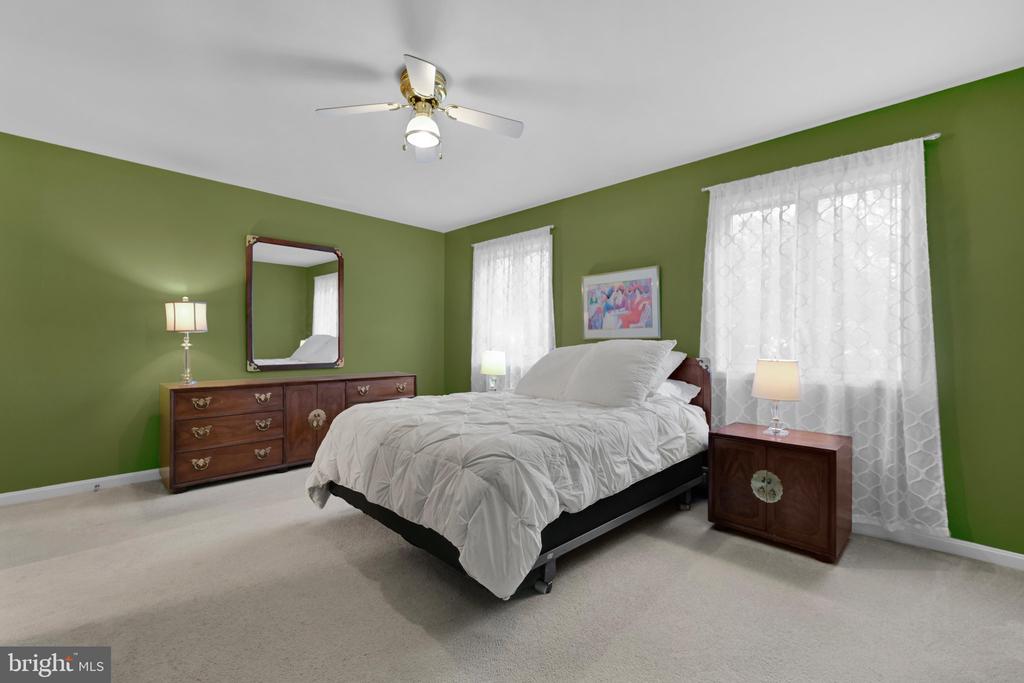 Bedroom with olive-green walls, a white bed, dark wood furniture, and sheer curtains.