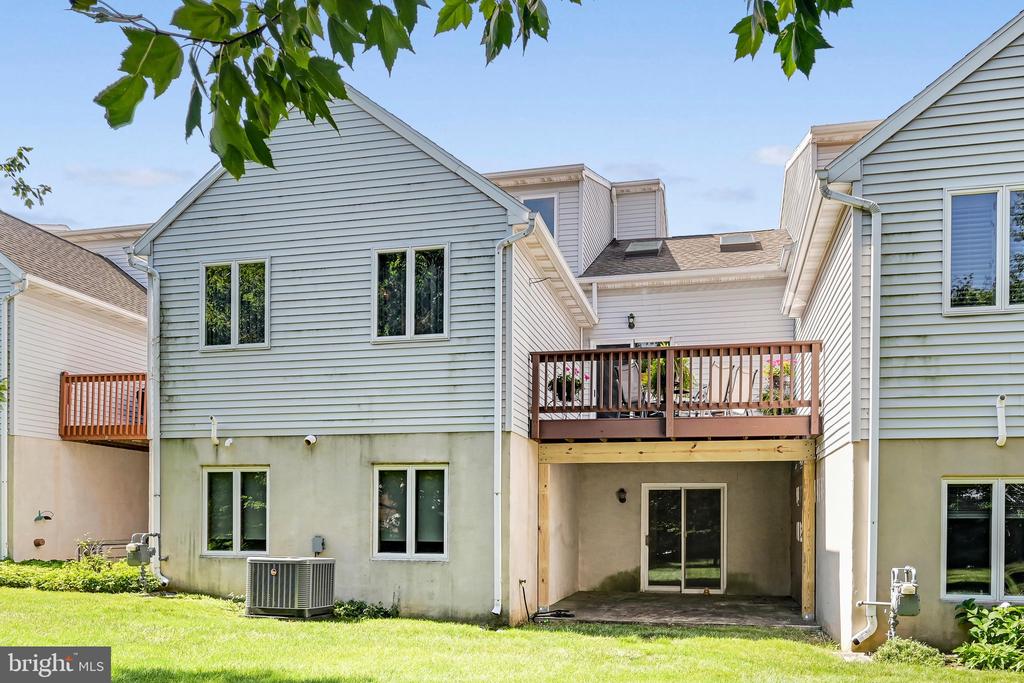Rear exterior of a home with an elevated deck, covered patio, and lawn.