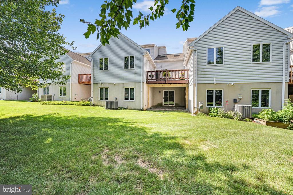 Rear exterior of attached homes with a central deck, covered patio, and broad lawn.