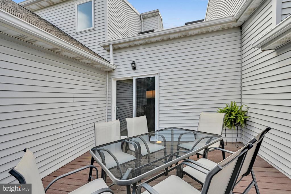 Enclosed deck with a glass-top dining table, chairs, sliding glass door, and potted fern.