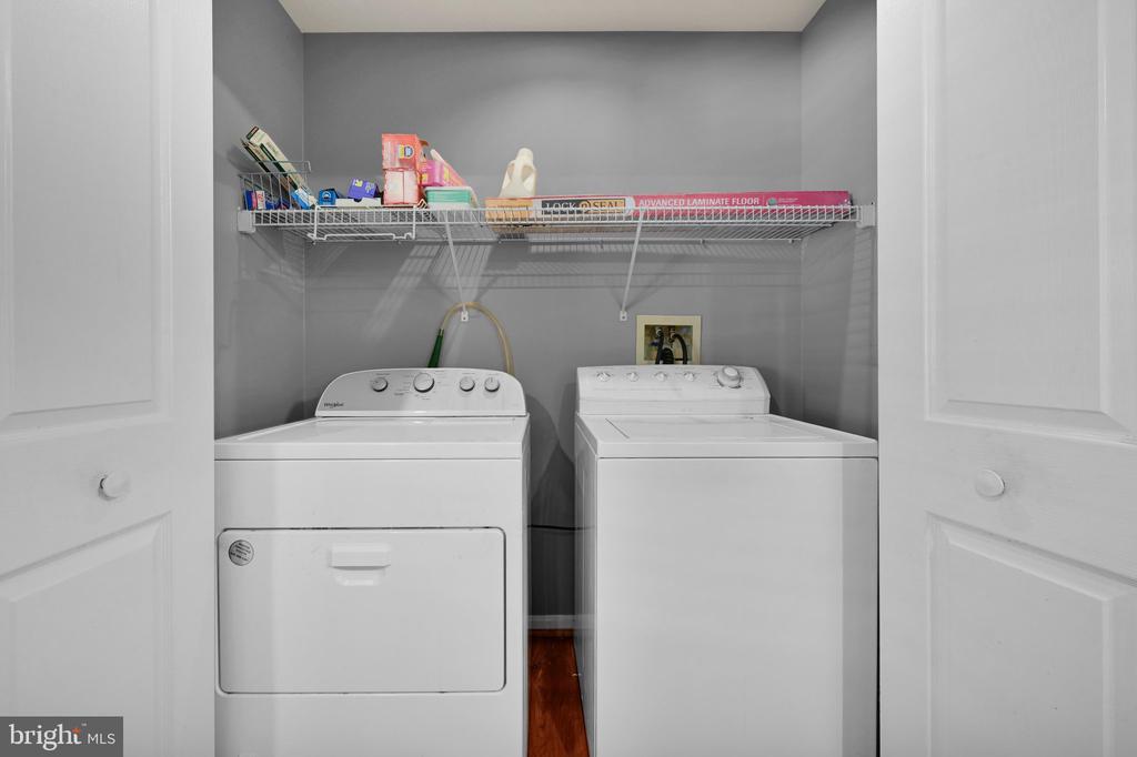 Laundry closet with white washer and dryer beneath a wire shelf.