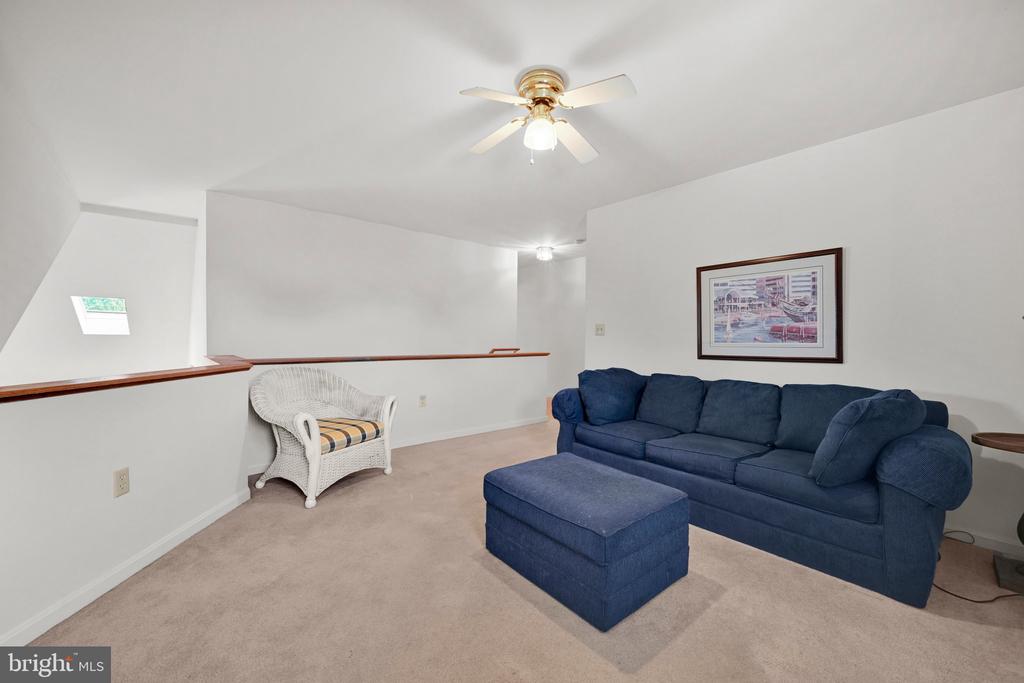 Living room with a navy sofa and ottoman, white wicker chair, and ceiling fan.