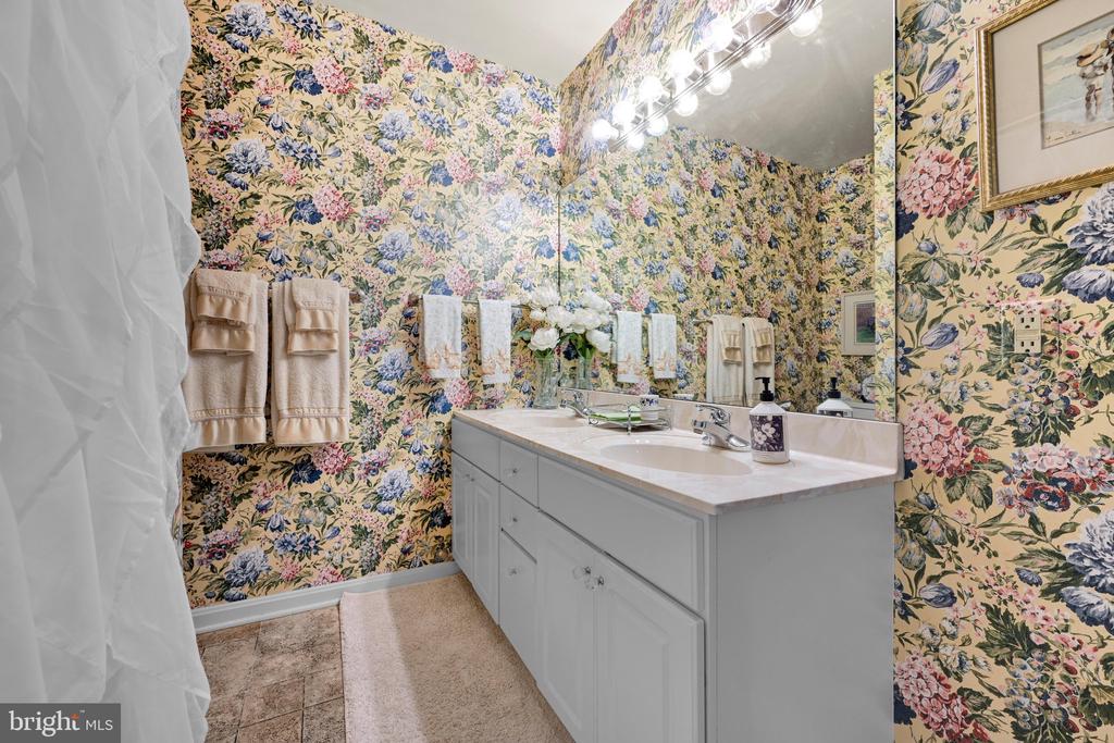 Bathroom with a white double vanity, large mirror, and colorful floral wallpaper.