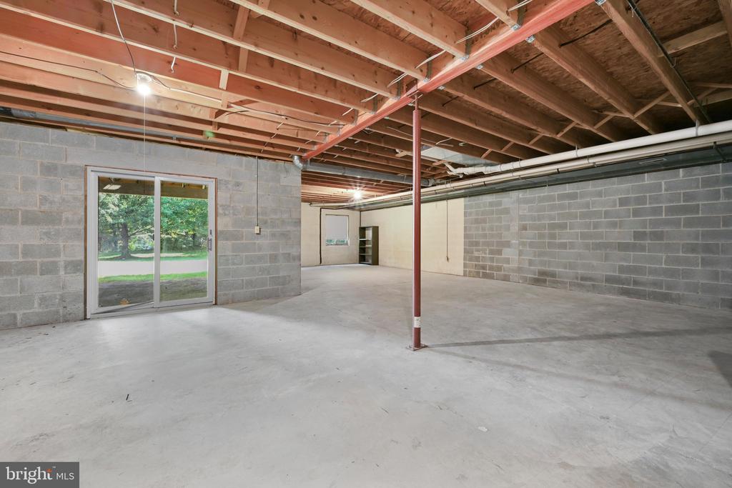 Unfinished basement with exposed ceiling joists, gray block walls, and a sliding glass door.