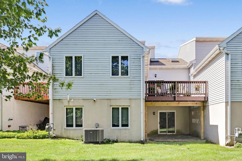 Townhouse rear with a raised wooden deck, covered patio, and grassy yard.