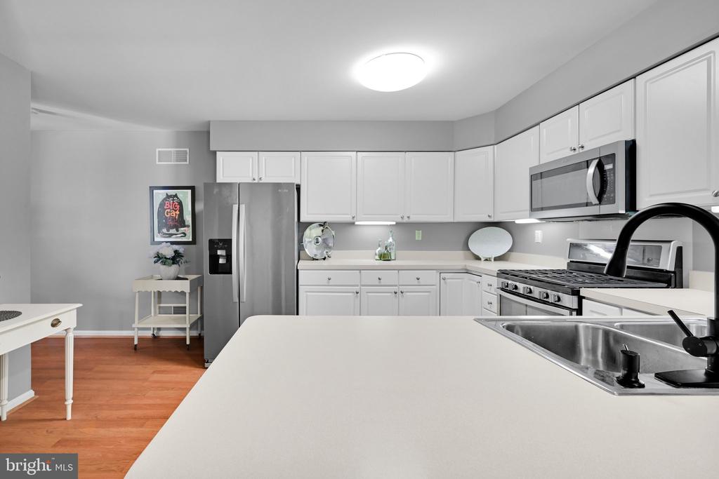 Kitchen with white cabinets, stainless steel appliances, a large island, and warm wood flooring.