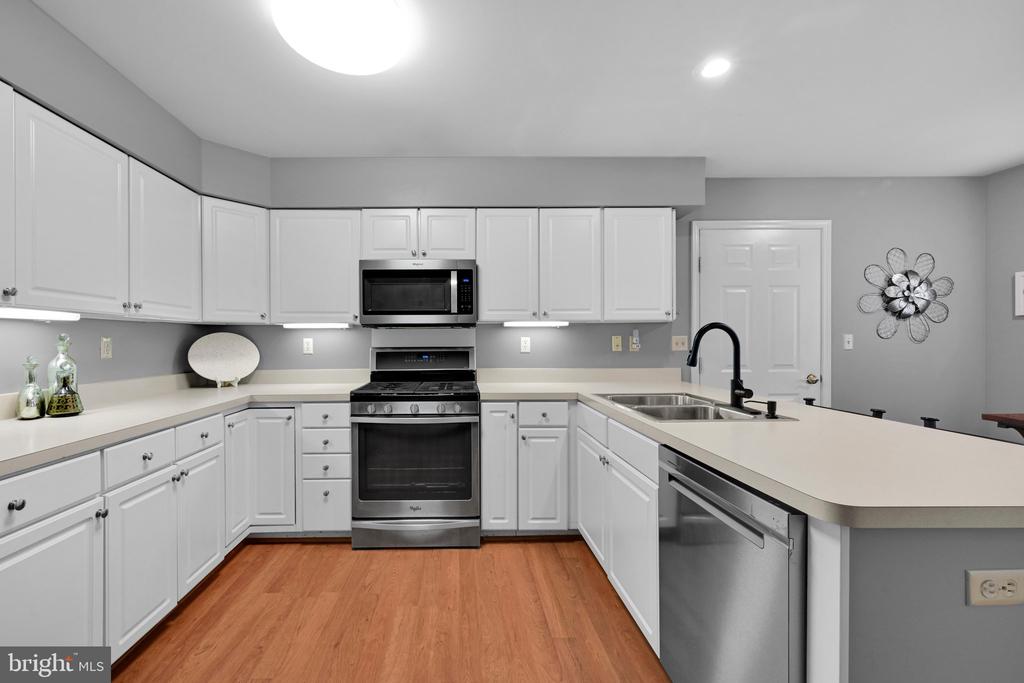 Renovated kitchen with white cabinets, stainless steel appliances, a double-basin sink, and warm wood flooring.