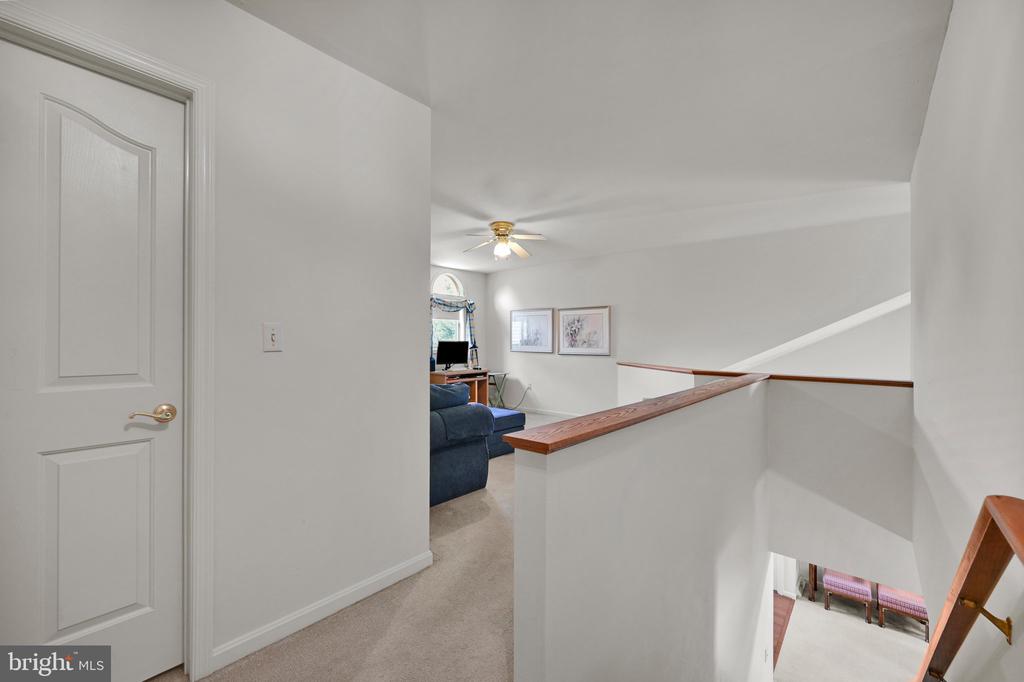 Upstairs landing with a wood-capped railing overlooking a sitting area with a blue sofa.