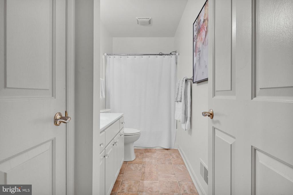 Bathroom with a white vanity, shower curtain, toilet, and peach-toned tile floor.